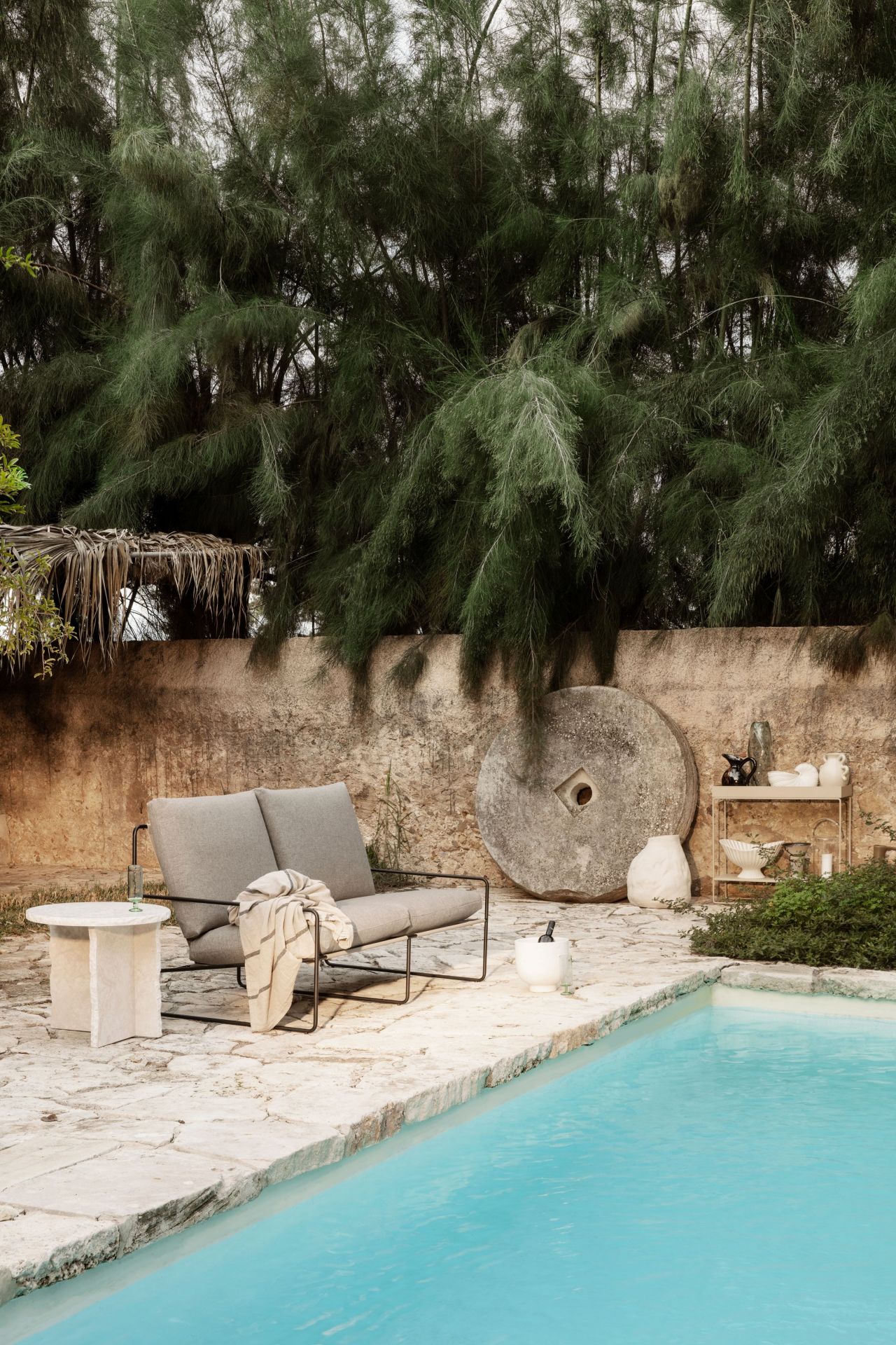 Desert 2-Sitzer Outdoor Sofa von Ferm Living mit schwarzem Gestell und gestreifter Decke am Pool.