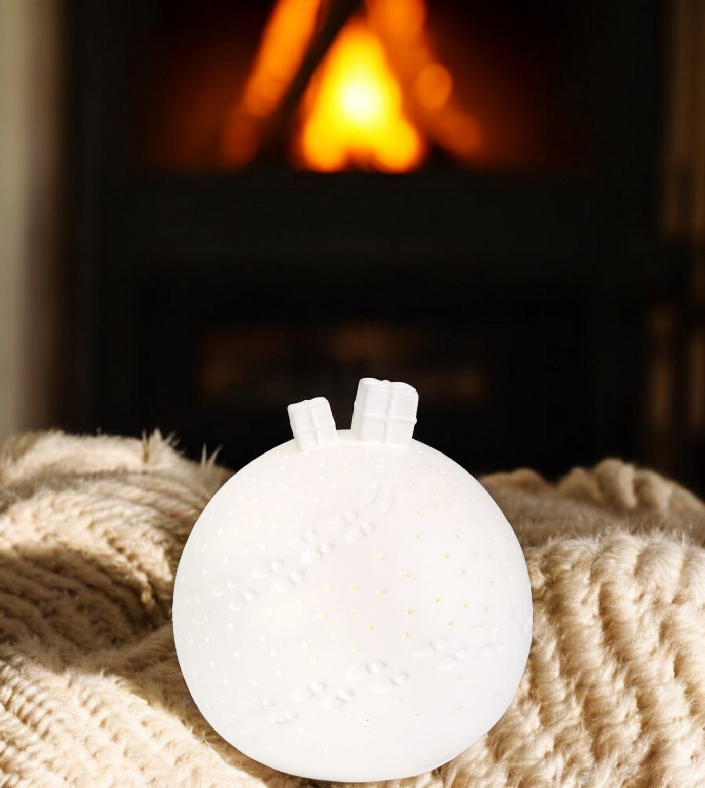 Weiße Porzellangeschichten Lichtkugel mit LED-Lichtern als Geschenkidee vor Kaminfeuer.