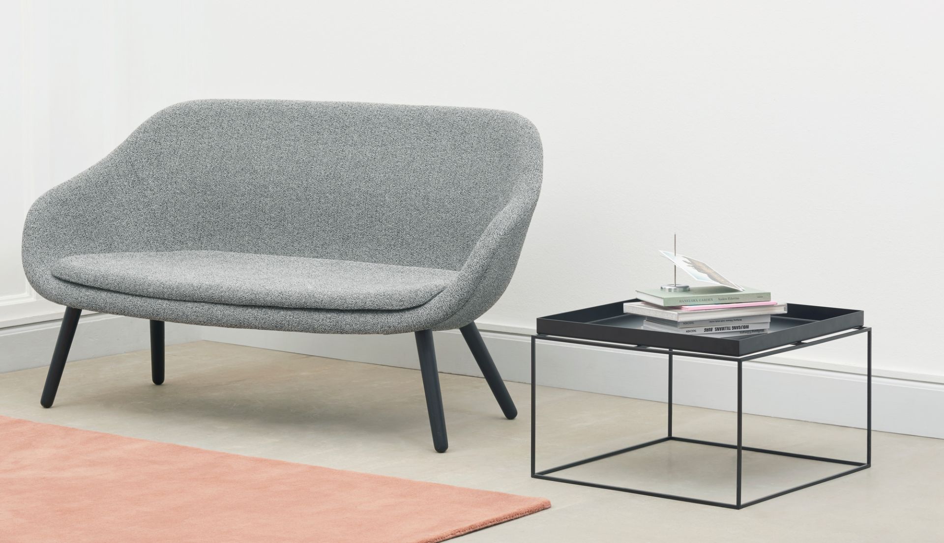 Grauer Sessel neben schwarzem Hay Tray Table Couchtisch mit Büchern und Dekoration in minimalistischem Wohnzimmer.