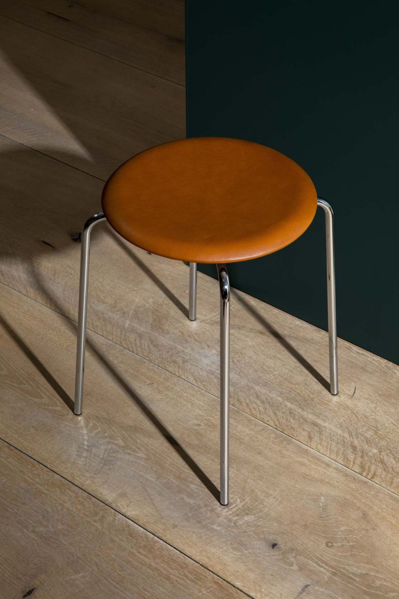 Dot Hocker von Fritz Hansen mit braunem Lederbezug und Chromgestell auf Holzboden. Design Hocker.