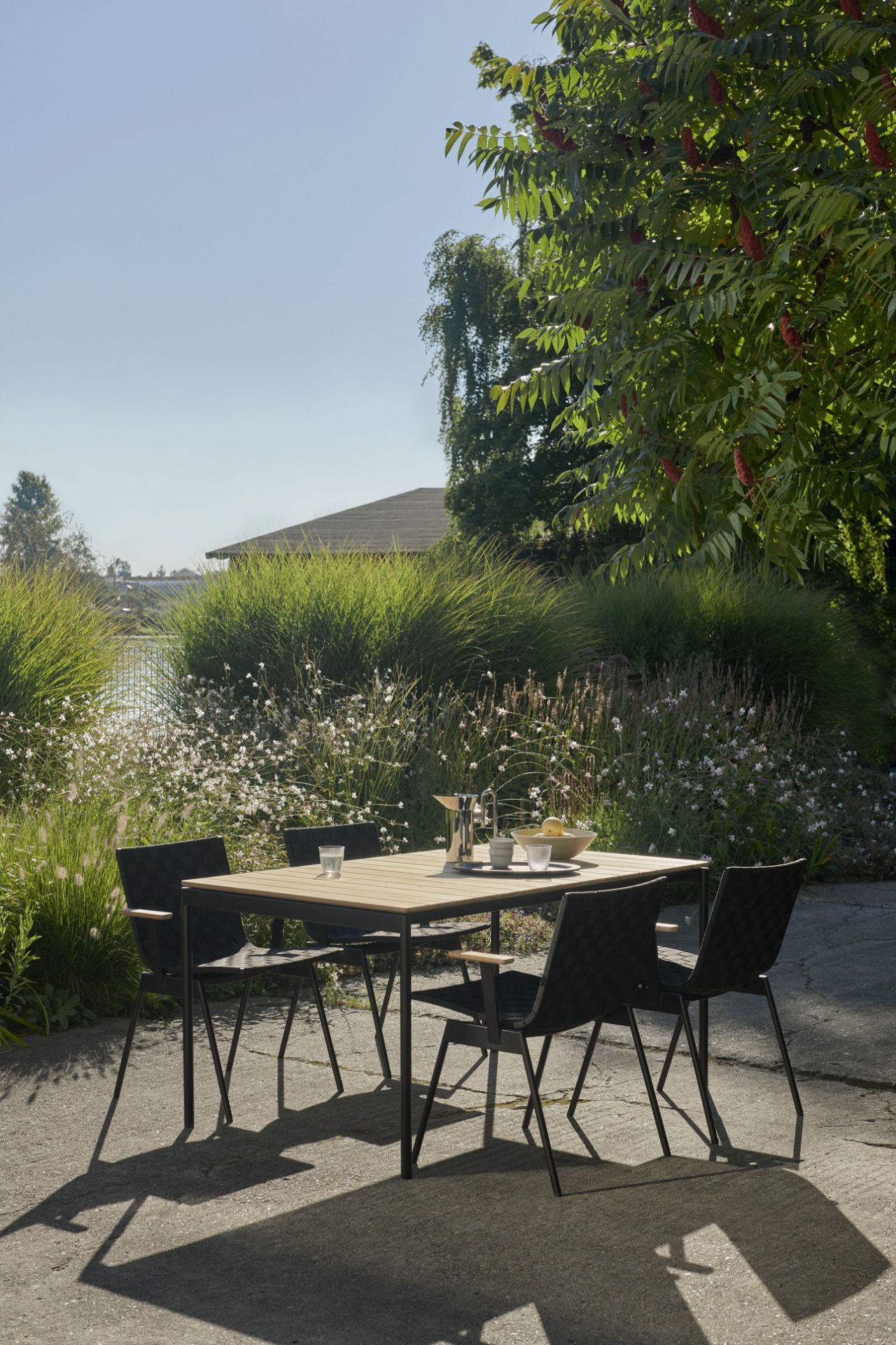 AndTradition Ville AV25 Outdoor Tisch mit vier Stühlen im Garten, gedeckt mit Getränken und Obst.