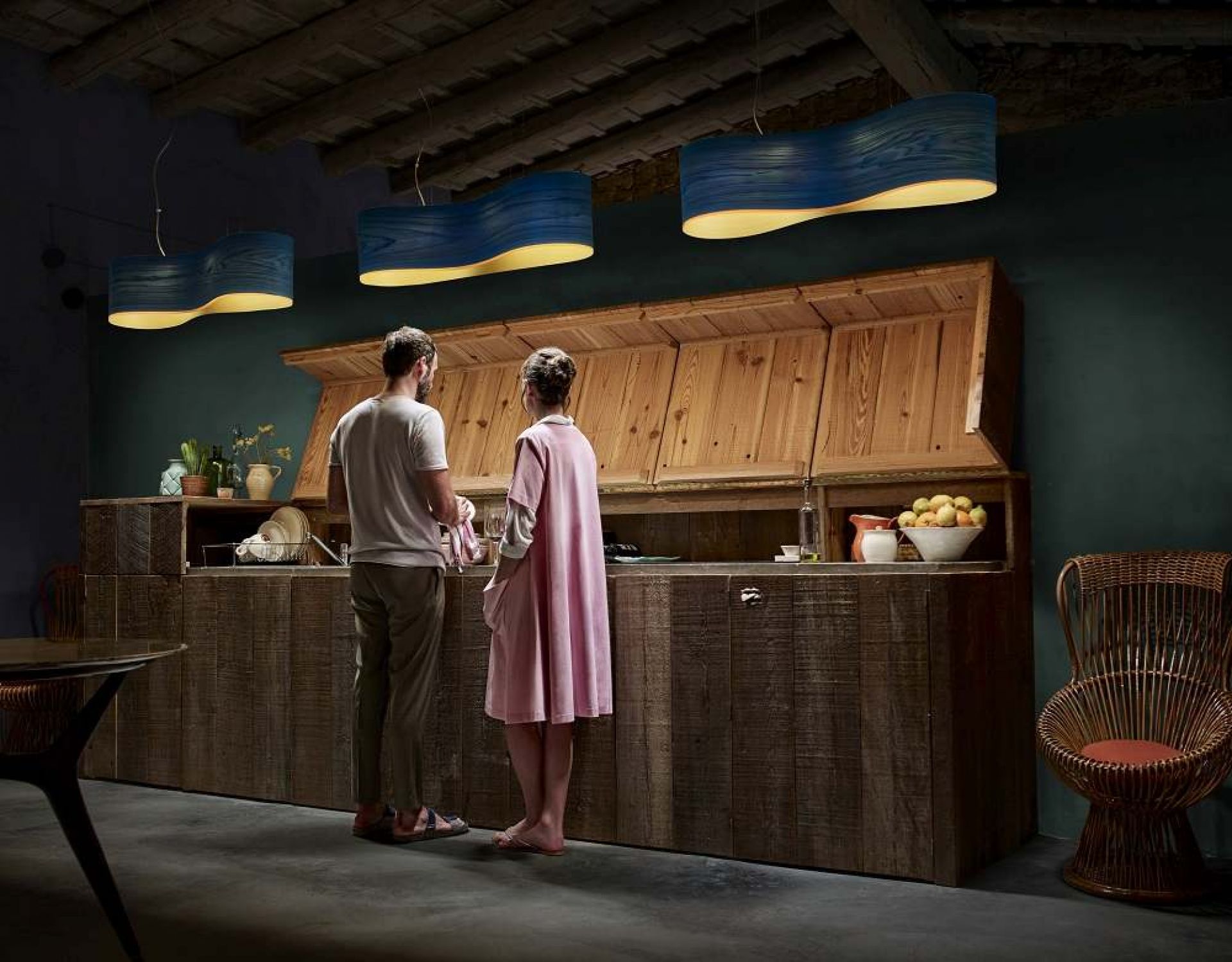 Blaue New Wave Pendelleuchten von LZF Lamps über einer rustikalen Holzküche mit zwei Personen.