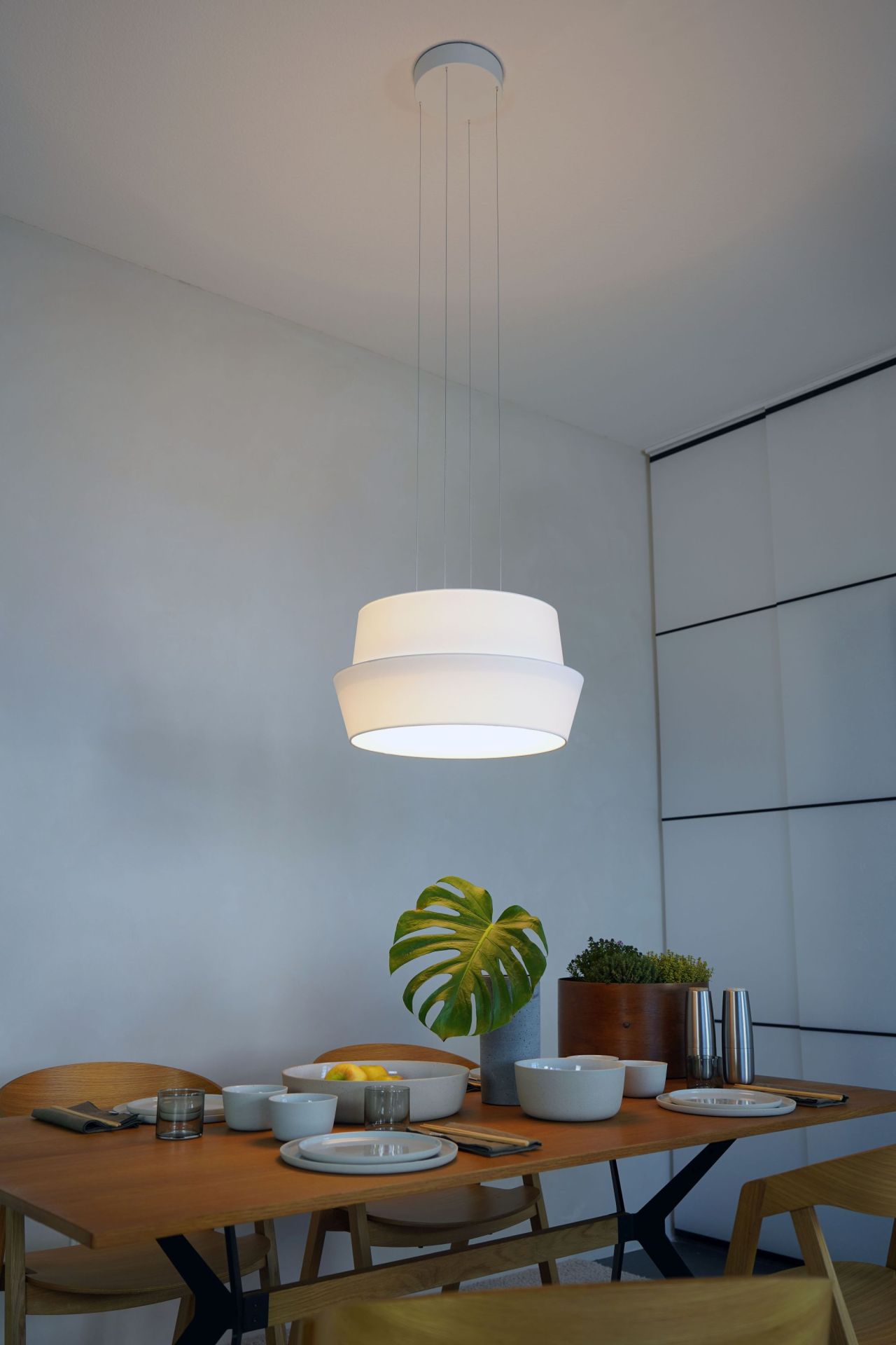 Weiße Fly Pendelleuchte von Maigrau über Esstisch mit Geschirr und Pflanzen. Moderne Hängelampe.