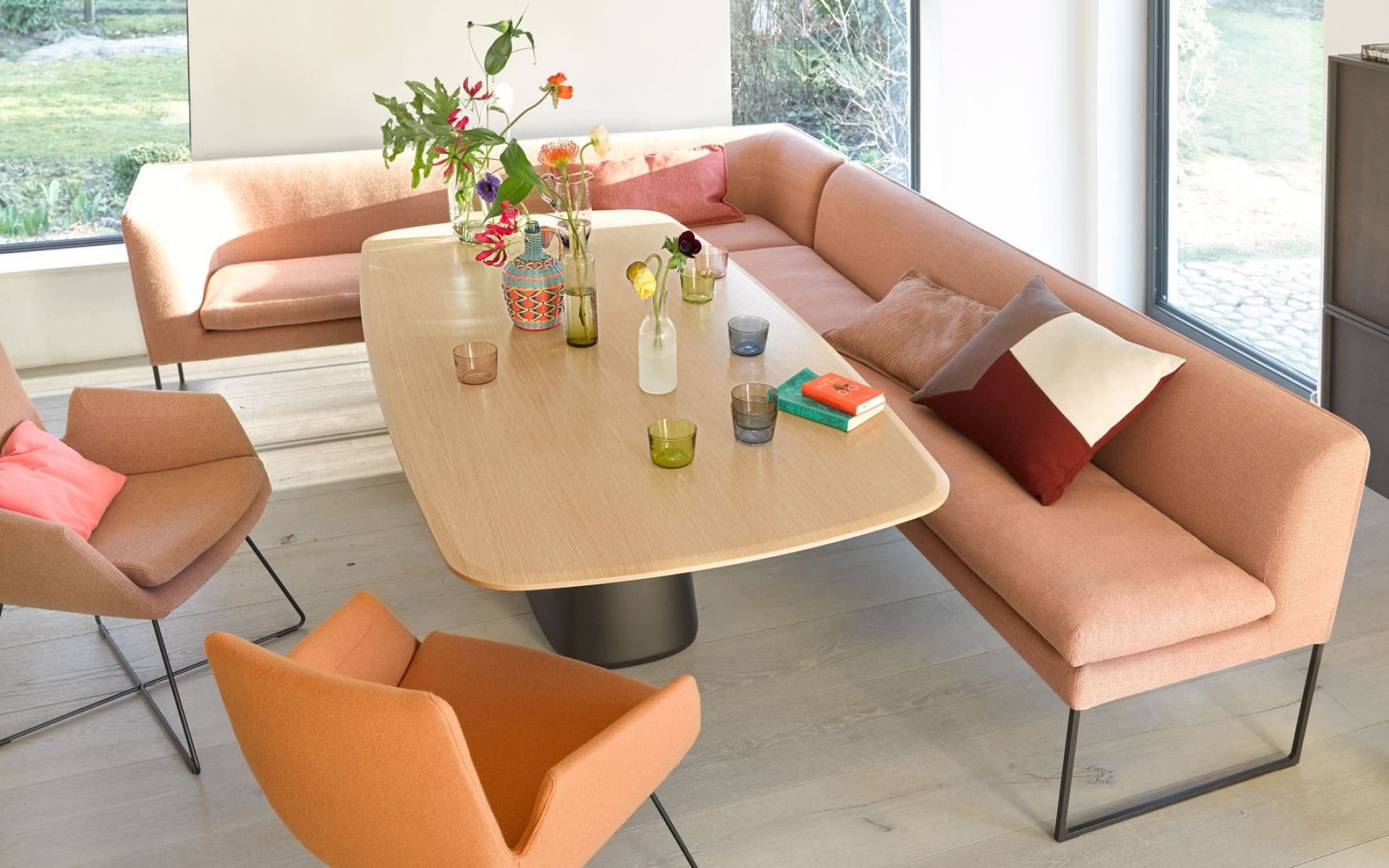 Heller Raum mit Conic Tisch, rosa Eckbank, Sesseln und Dekoration. Modernes Esszimmer-Interieur.