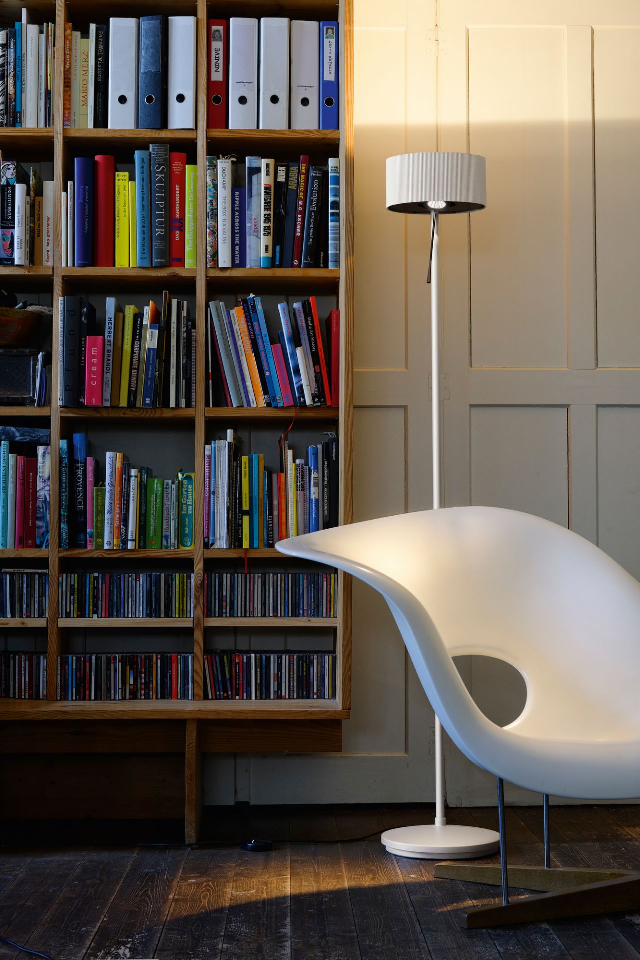 Diogenes LED Stehleuchte von Belux in Goldgrau neben Bücherregal und Design-Sessel. Moderne Beleuchtung.