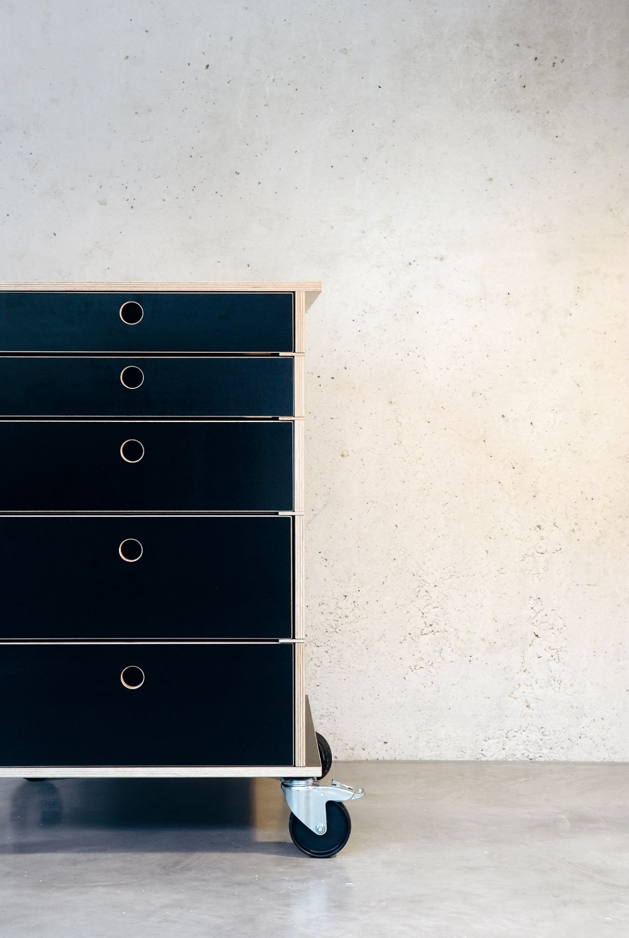 Schwarzer Lader Schubladenschrank von Nils Holger Moormann mit fünf Schubladen und Rollen vor Betonwand.