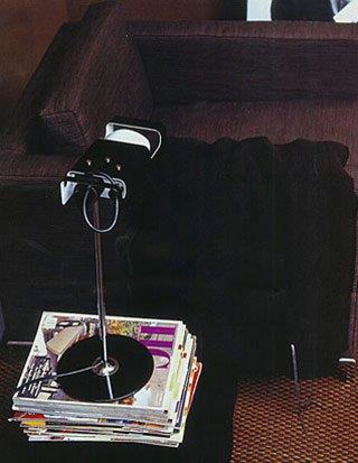 Schwarze Oluce Spider Tischleuchte auf einem Stapel Zeitschriften neben einem Sofa.