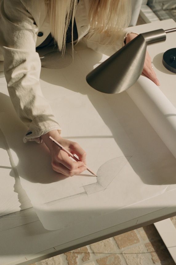 Frau zeichnet Skizze einer MS Series Tischleuchte von Fritz Hansen mit Bleistift.