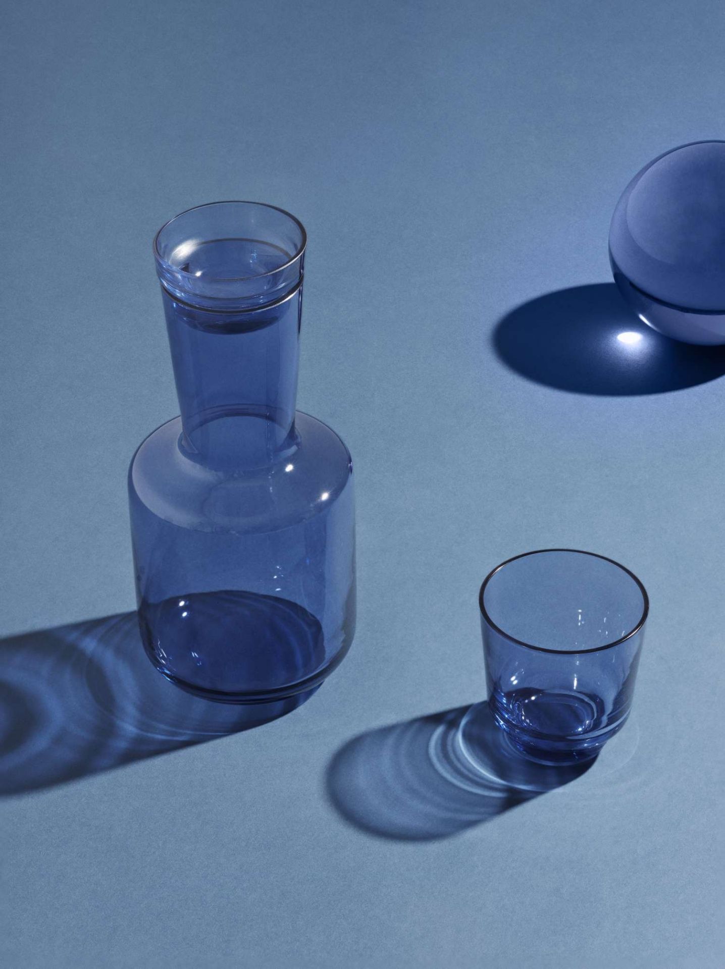 Blaue Raise Karaffe von Muuto mit passendem Glas auf blauem Hintergrund.