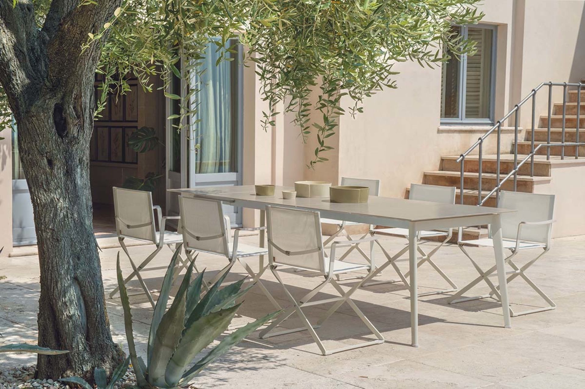 Weißer Ciak Regiestuhl von Emu neben einem Gartentisch im Außenbereich unter einem Olivenbaum.