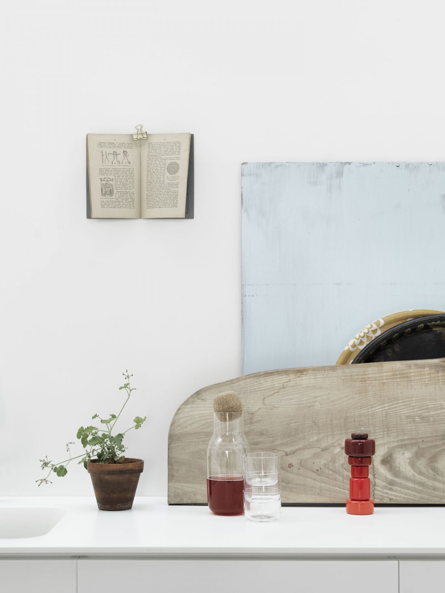 Stillleben mit Corky Karaffe, Glas, Pflanze und Buch auf weißer Oberfläche. Muuto Design.