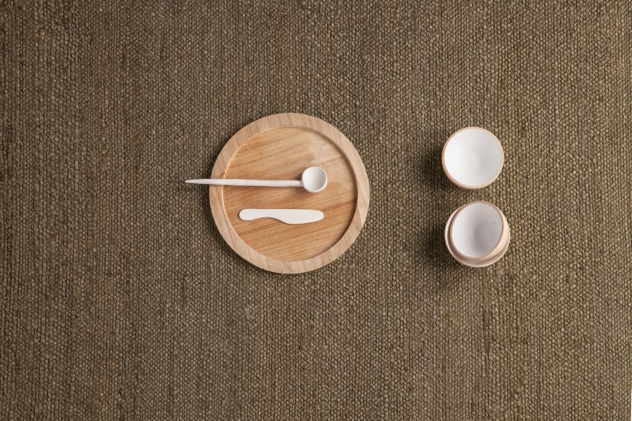 Detailaufnahme des braunen Herb Teppichs von Nanimarquina mit Holztablett und Keramikschalen.