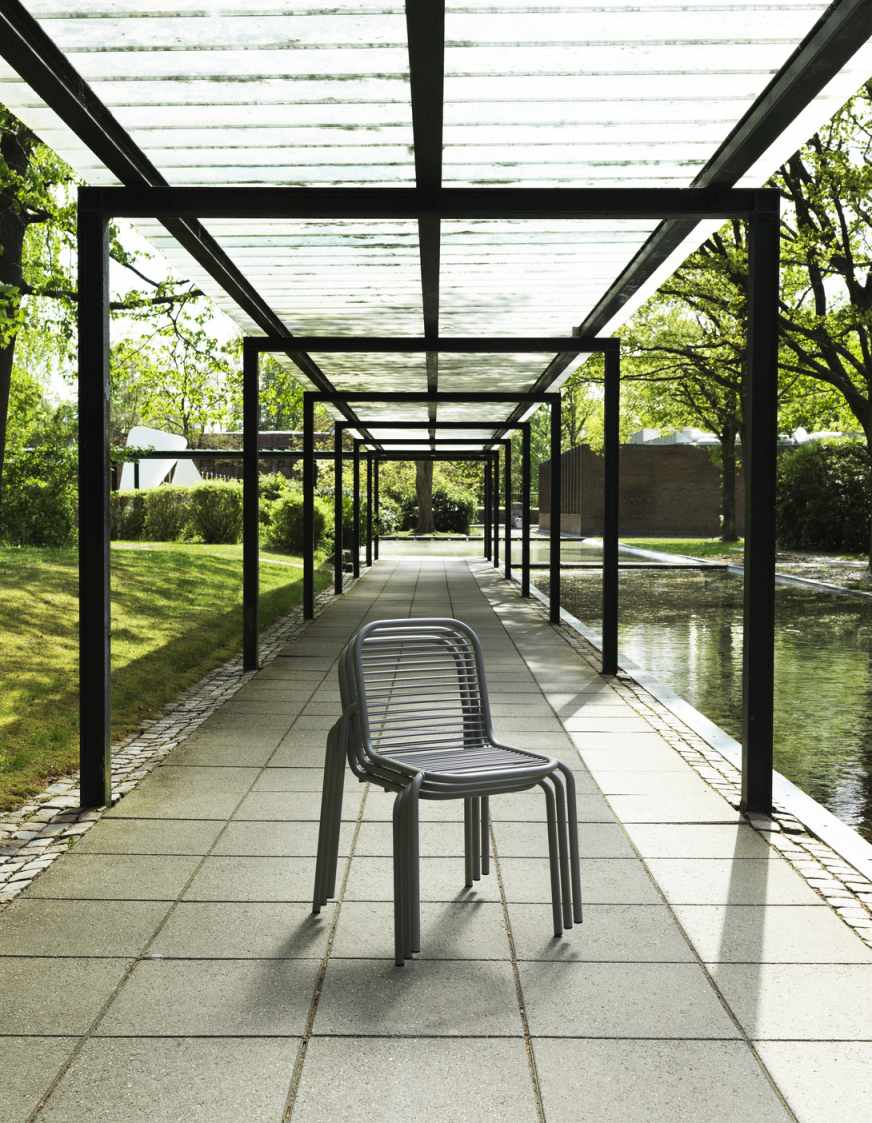 Normann Copenhagen Vig Chair Outdoor: Grauer Stapelstuhl aus Metall unter einer Pergola im Park.