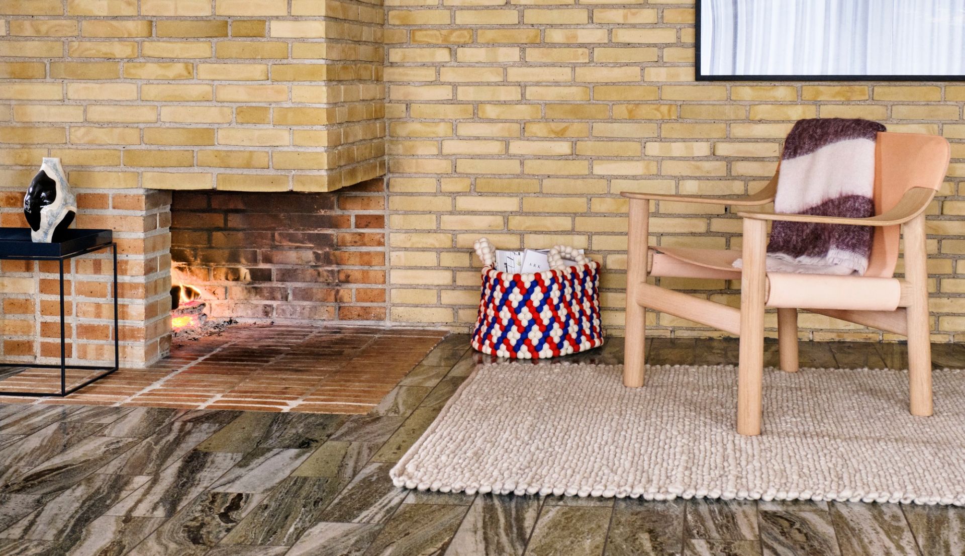 Nahaufnahme des Peas Teppichs in Beige, vor Kamin und Holzstuhl, gemütliches Wohnambiente.
