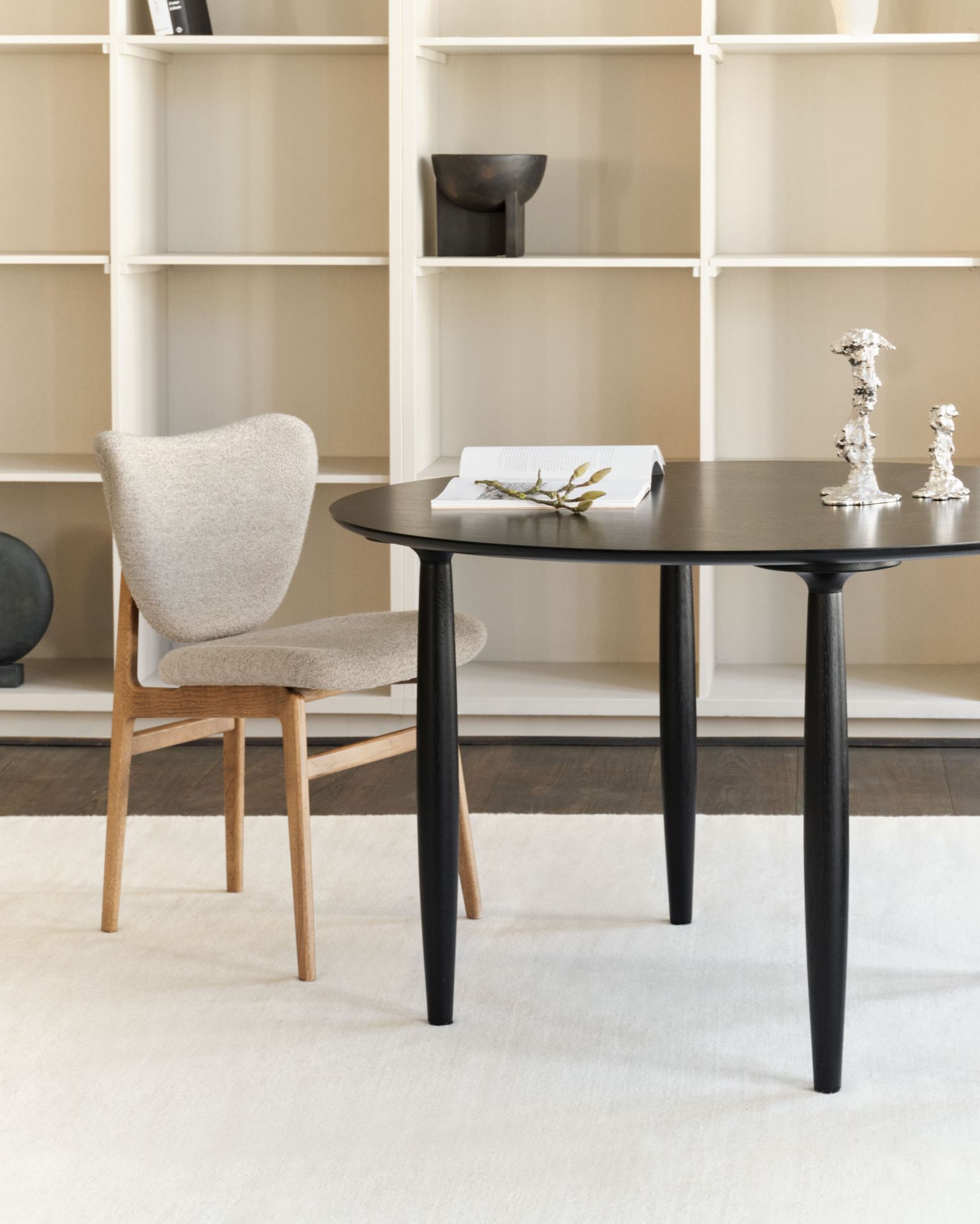 Oku Esstisch rund Eiche schwarz von Norr11 mit Stuhl und Dekoration vor Regal.