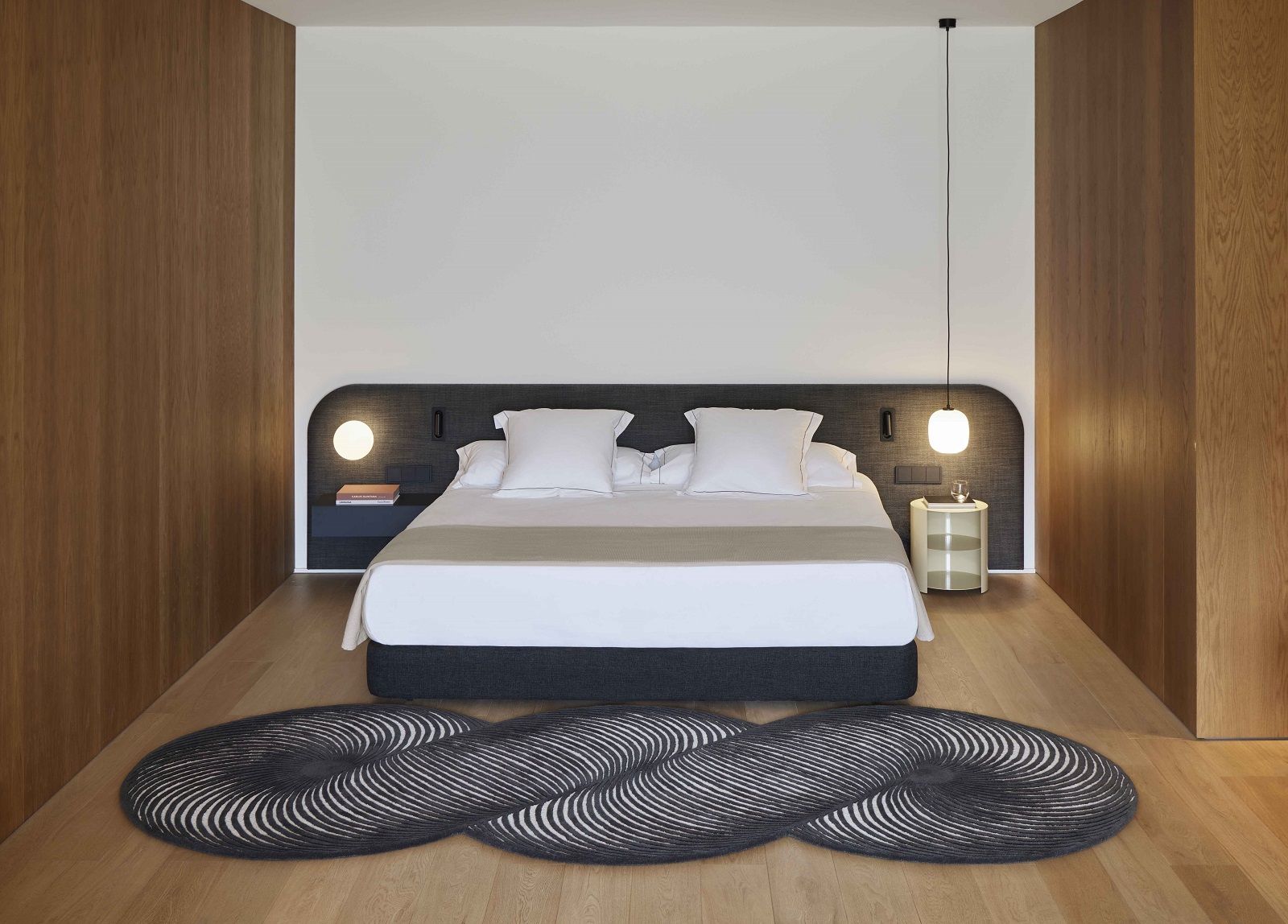 Schlafzimmer mit Bett und dem schwarzen Giro Teppich von Gan mit auffälligem, gewebtem Design.