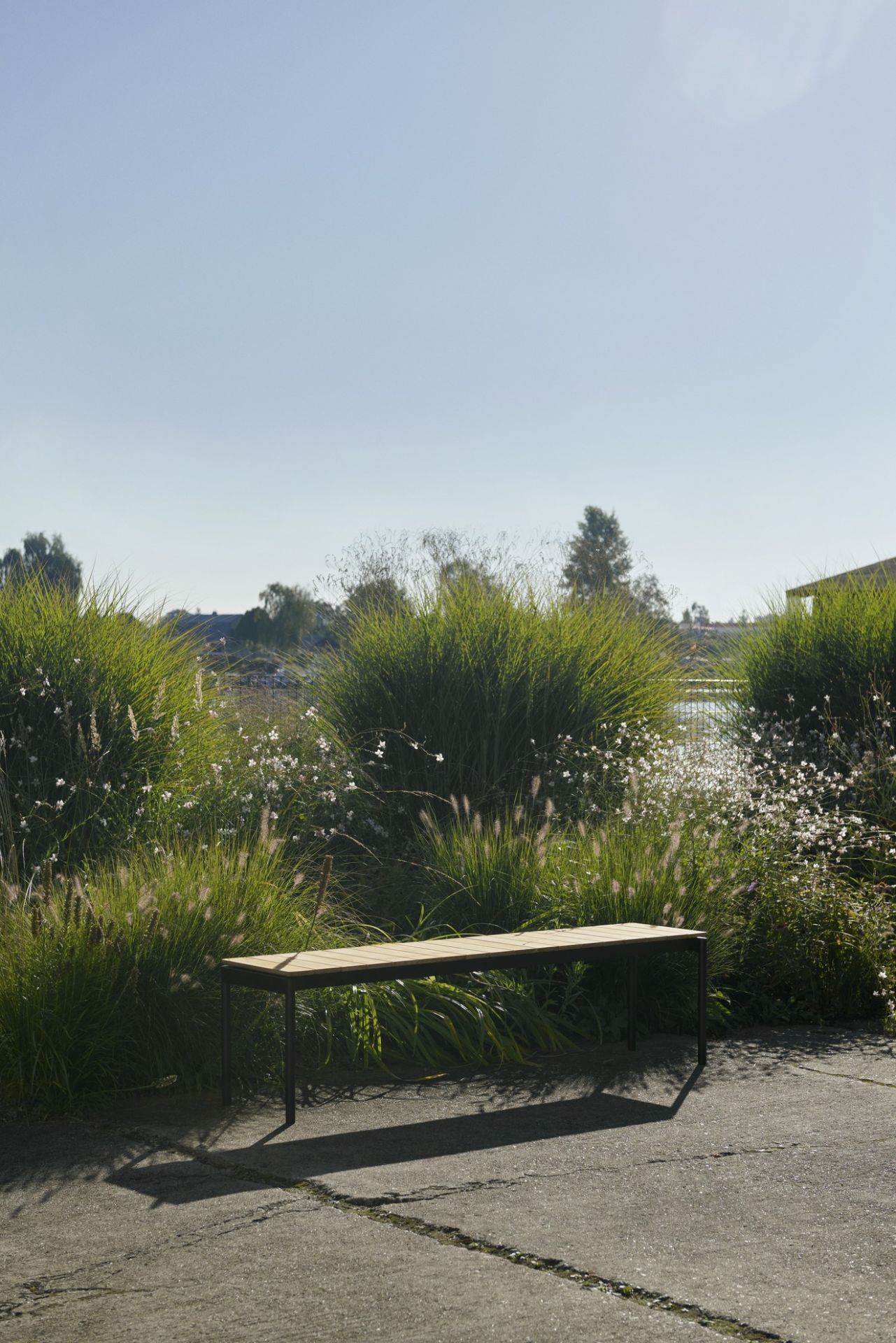 AndTradition Ville AV28 Gartenbank aus Holz und Metall vor üppigem Grün im Außenbereich.