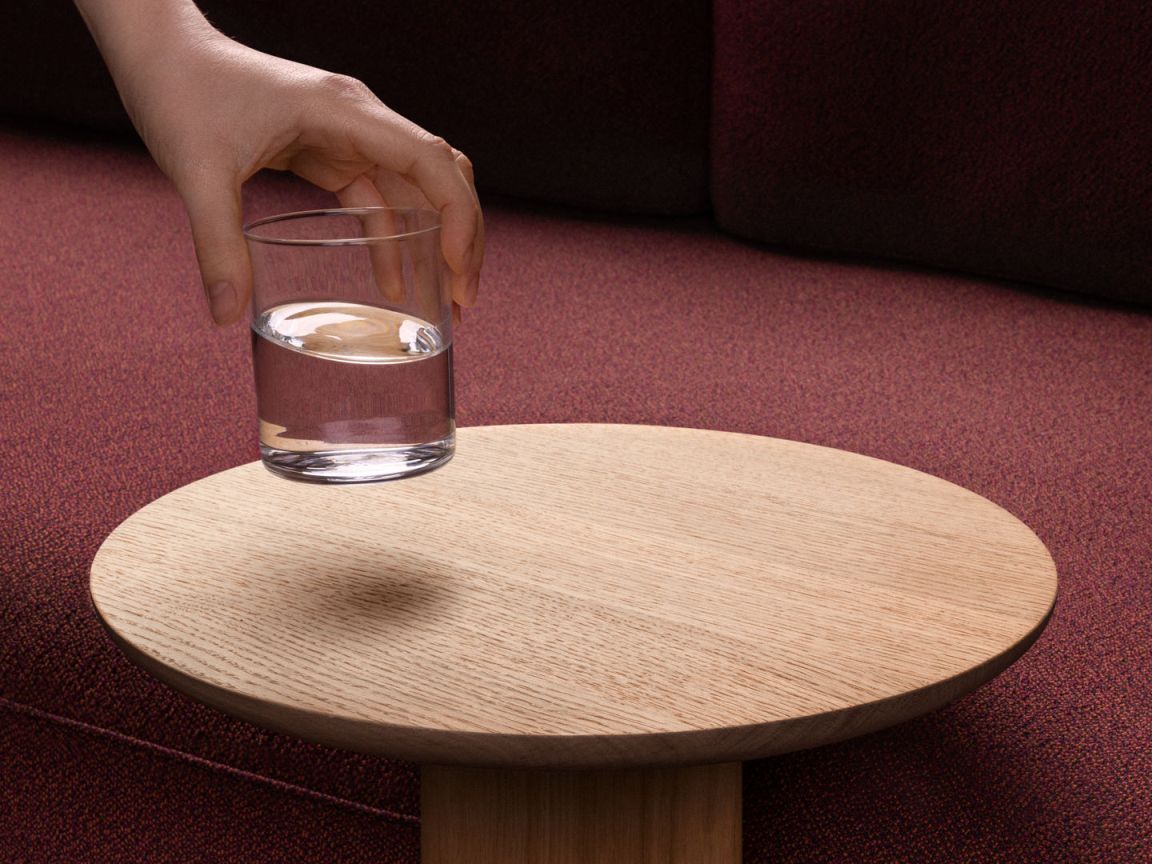 Nahaufnahme des runden Vitra Anagram Anstecktisches aus Holz mit einem Wasserglas darauf.