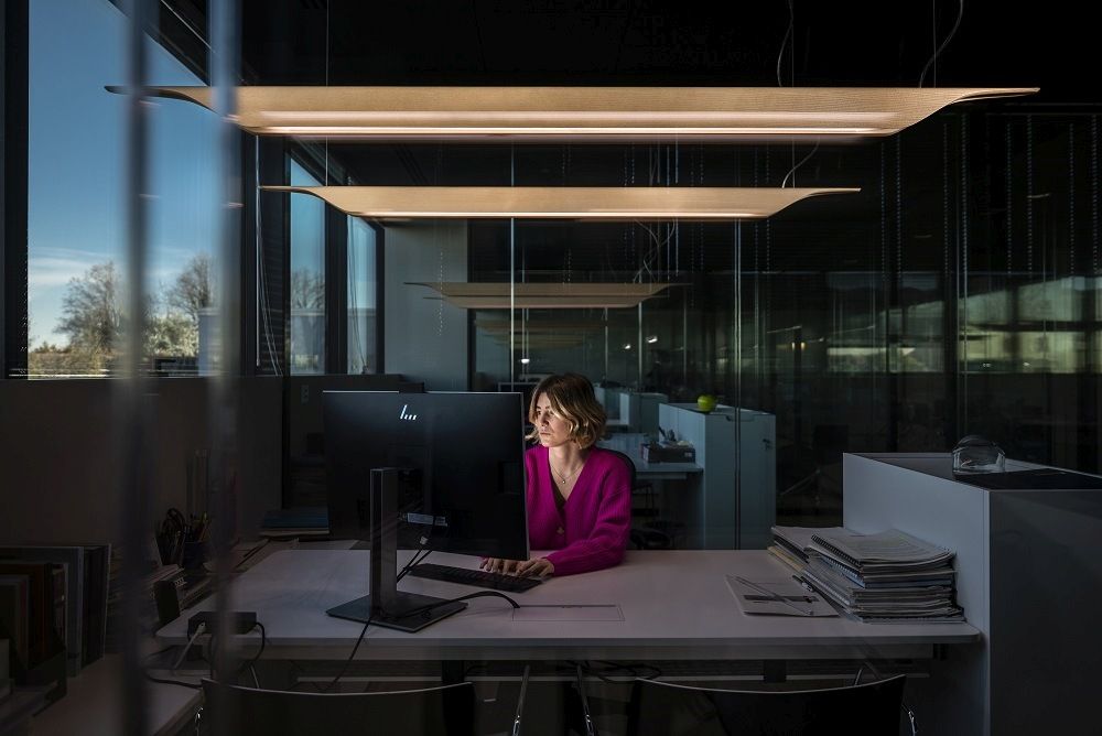 Frau arbeitet unter der Foscarini Troag Media LED Hängeleuchte im Büro, modernes Design.