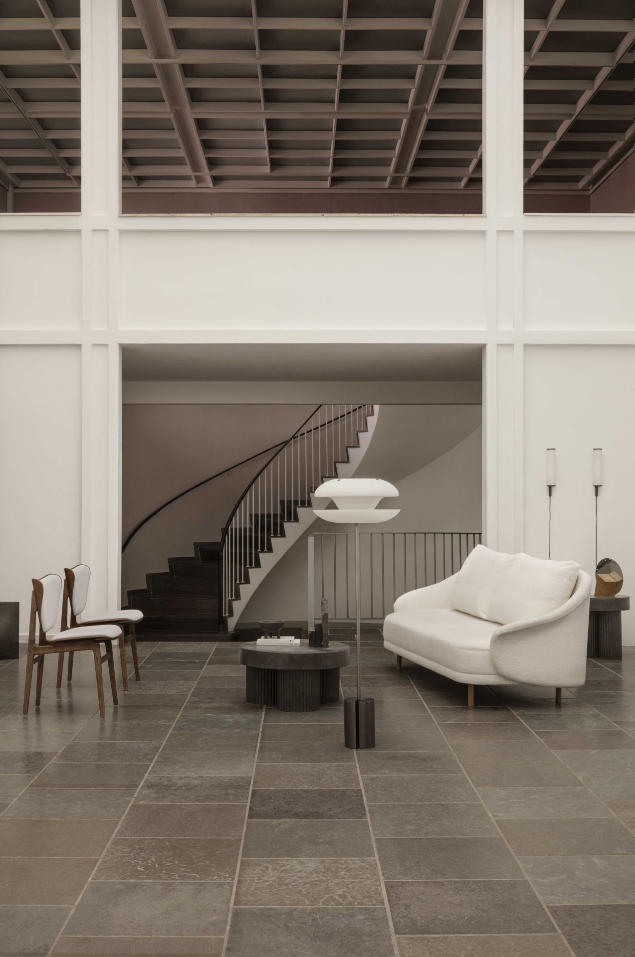 Norr11 Gear Beistelltisch aus dunklem Travertin in modernem Wohnzimmer mit Sofa und Treppe.