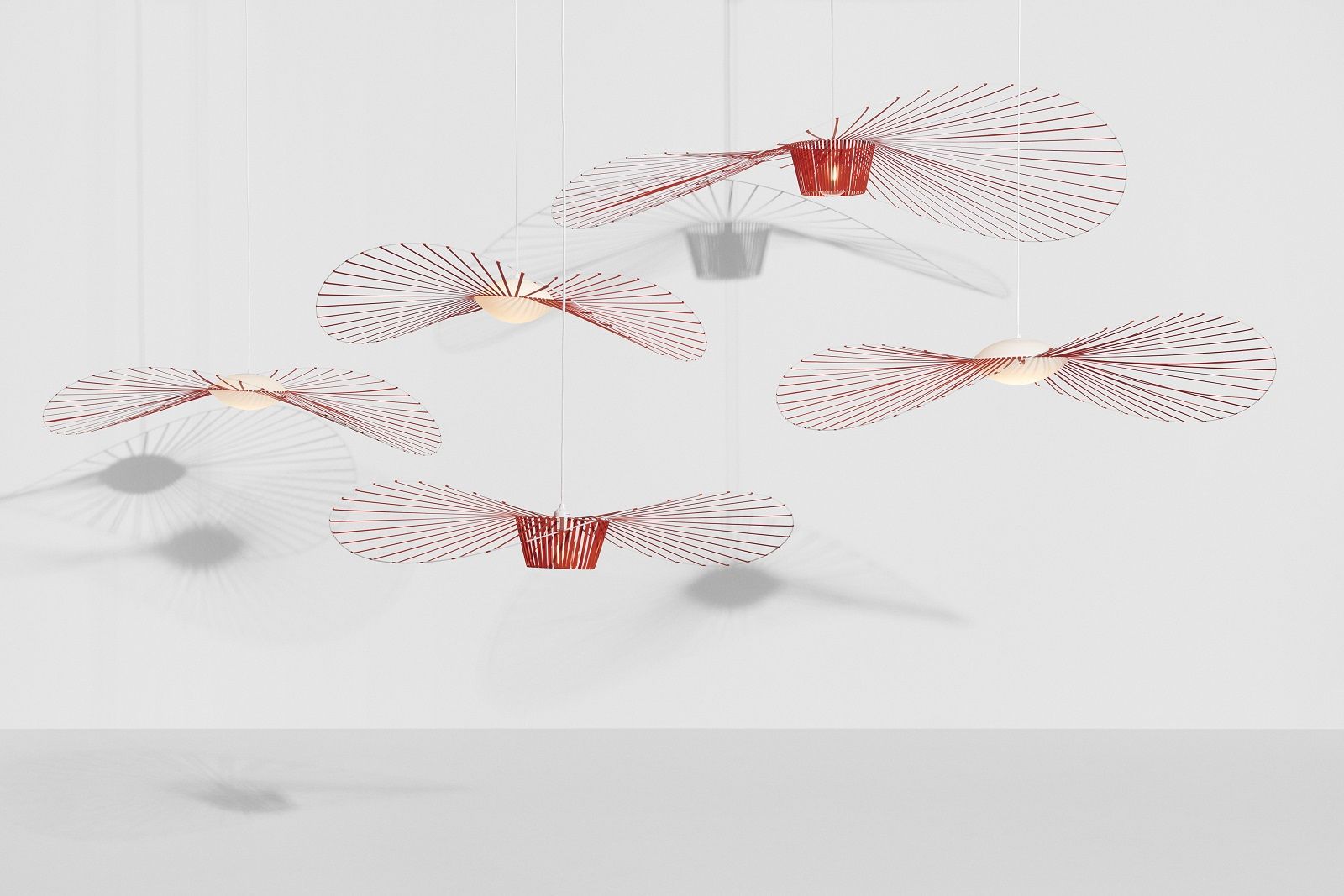 Mehrere rote Vertigo Nova Pendelleuchten von Petite Friture hängen an weißen Kabeln vor weißem Hintergrund.