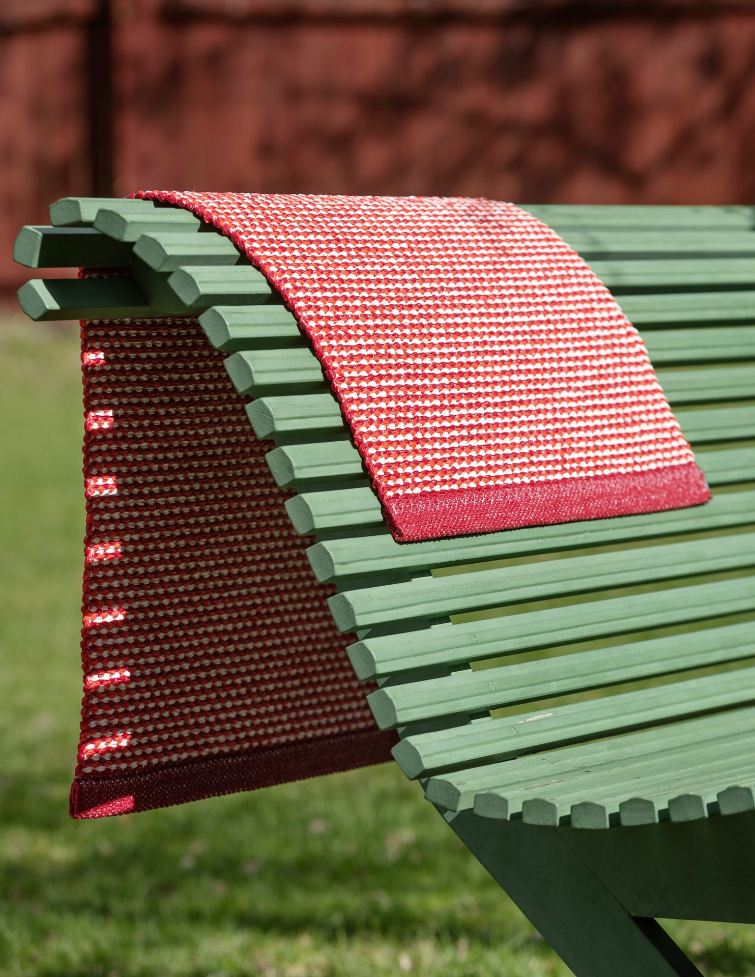 Effi Kunststoffteppich von Pappelina, 70x200 cm, rot-weiß gestreift, auf einer grünen Gartenbank. Outdoor Teppich.