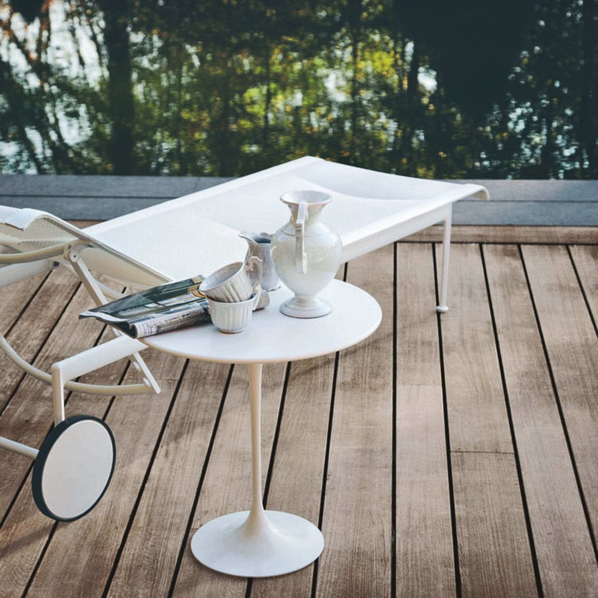 Weiße Richard Schultz Outdoor Liege und Beistelltisch auf Holzterrasse mit Blick auf Wasser.