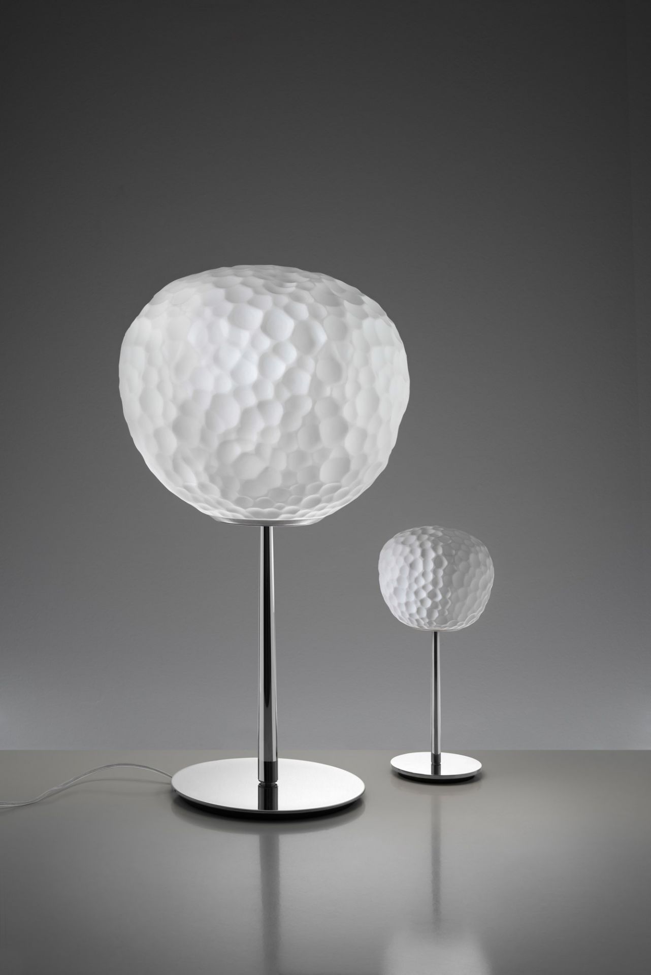 Meteorite Tischleuchte von Artemide: Zwei moderne Lampen mit strukturiertem, weißem Glas und Chromfuß.