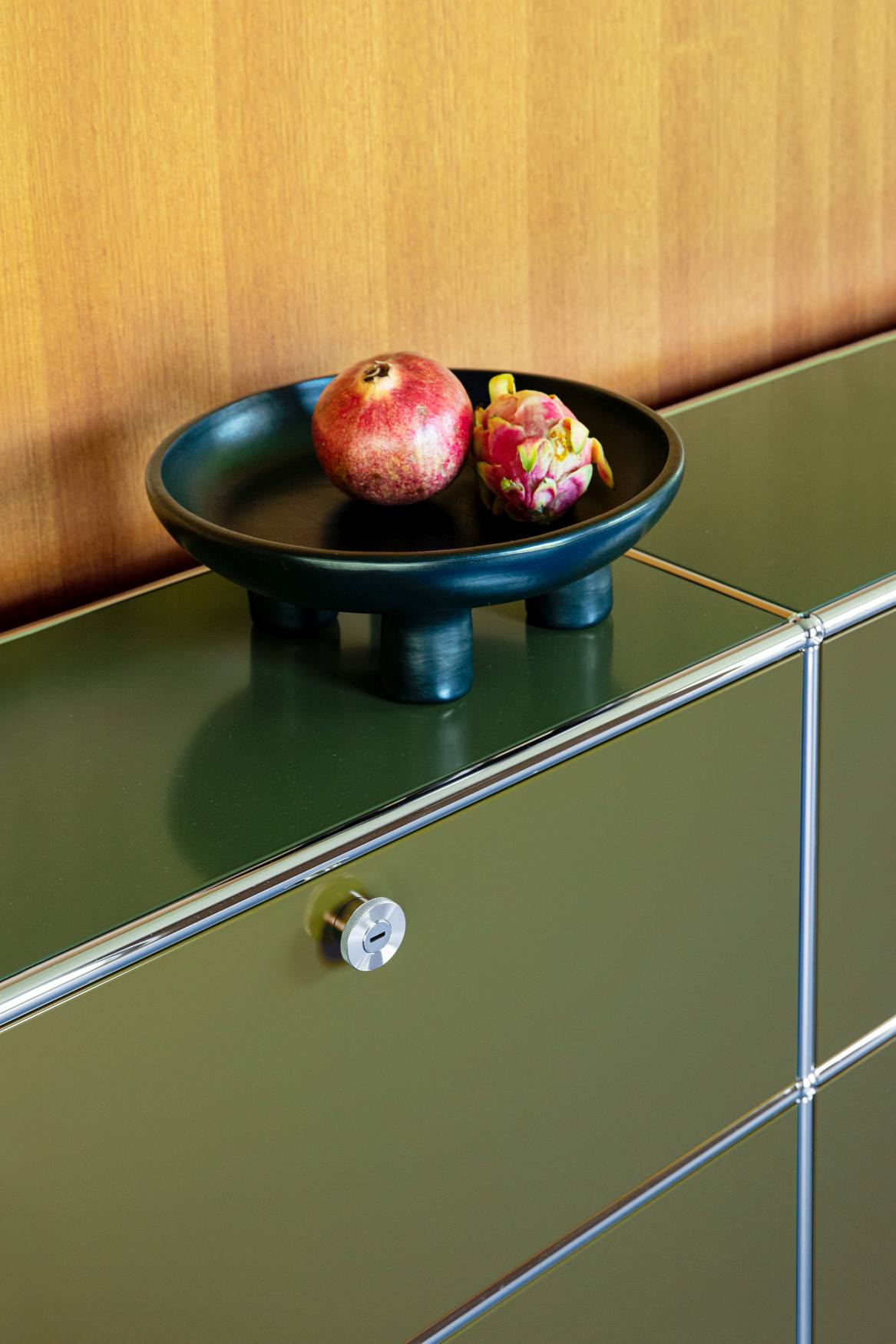 USM Haller Sideboard in Olivgrün mit vier Klapptüren, dekoriert mit Schale und Früchten.