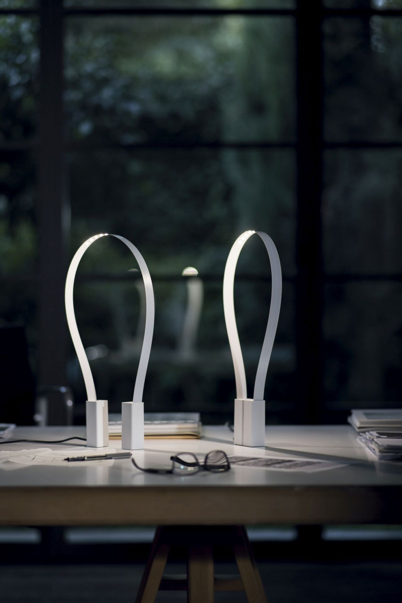 Zwei moderne Martinelli Luce Fluida Tischleuchten auf einem Schreibtisch mit Brille und Stift.