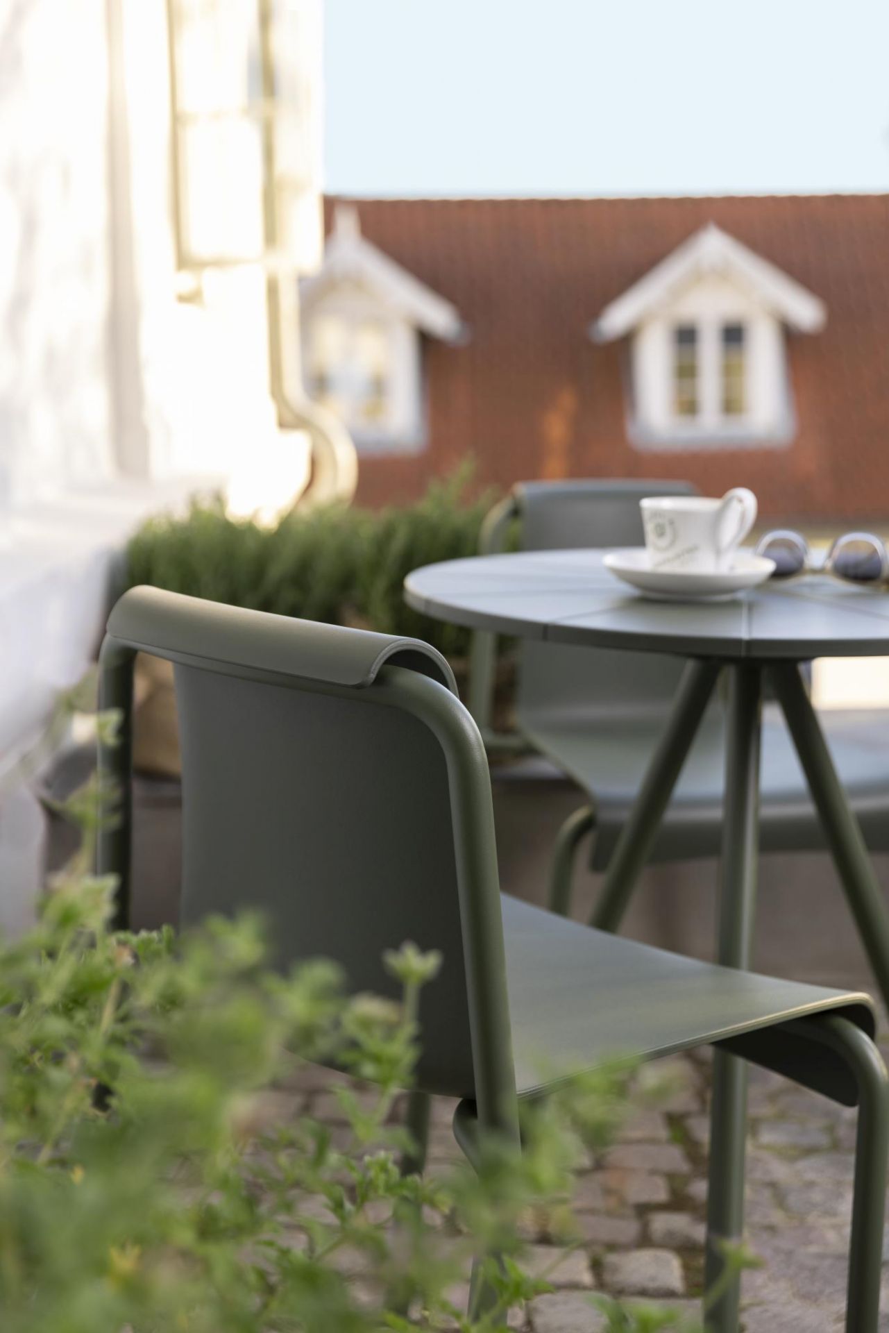 Nahaufnahme eines grünen Houe Nami Dining Chair Outdoor Stuhls mit Tisch auf einer Terrasse.