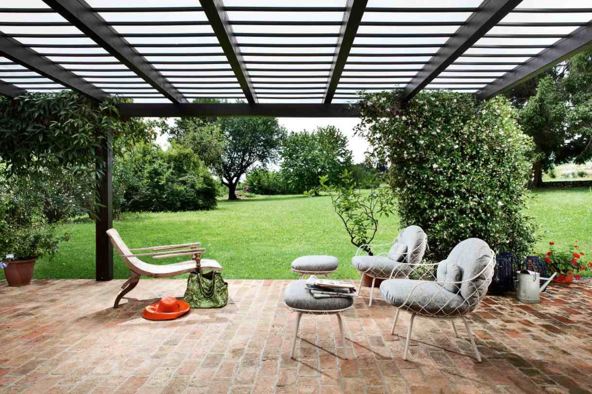 Piña Low Chair: Magis Outdoor Sessel auf einer Terrasse mit Garten im Hintergrund.