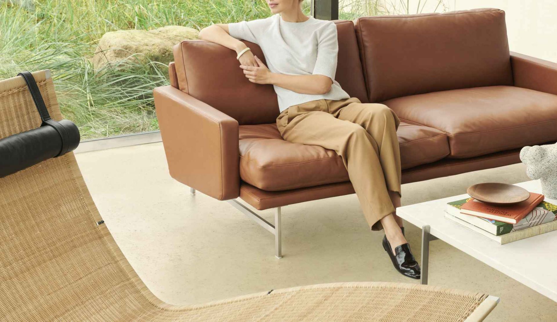 Frau entspannt auf braunem Ledersofa von Fritz Hansen, daneben die PK24 Liege. Hochwertige Designermöbel.
