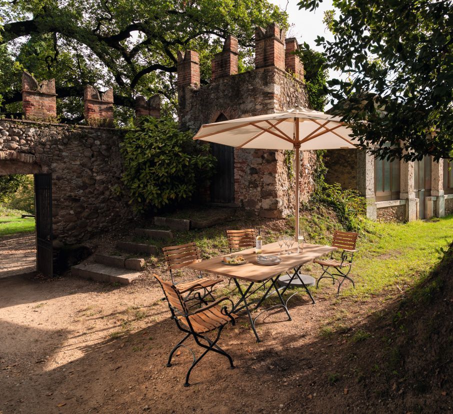 Weishäupl Classic Tisch 120 cm Outdoor, weiß, mit Stühlen und Sonnenschirm im Garten.