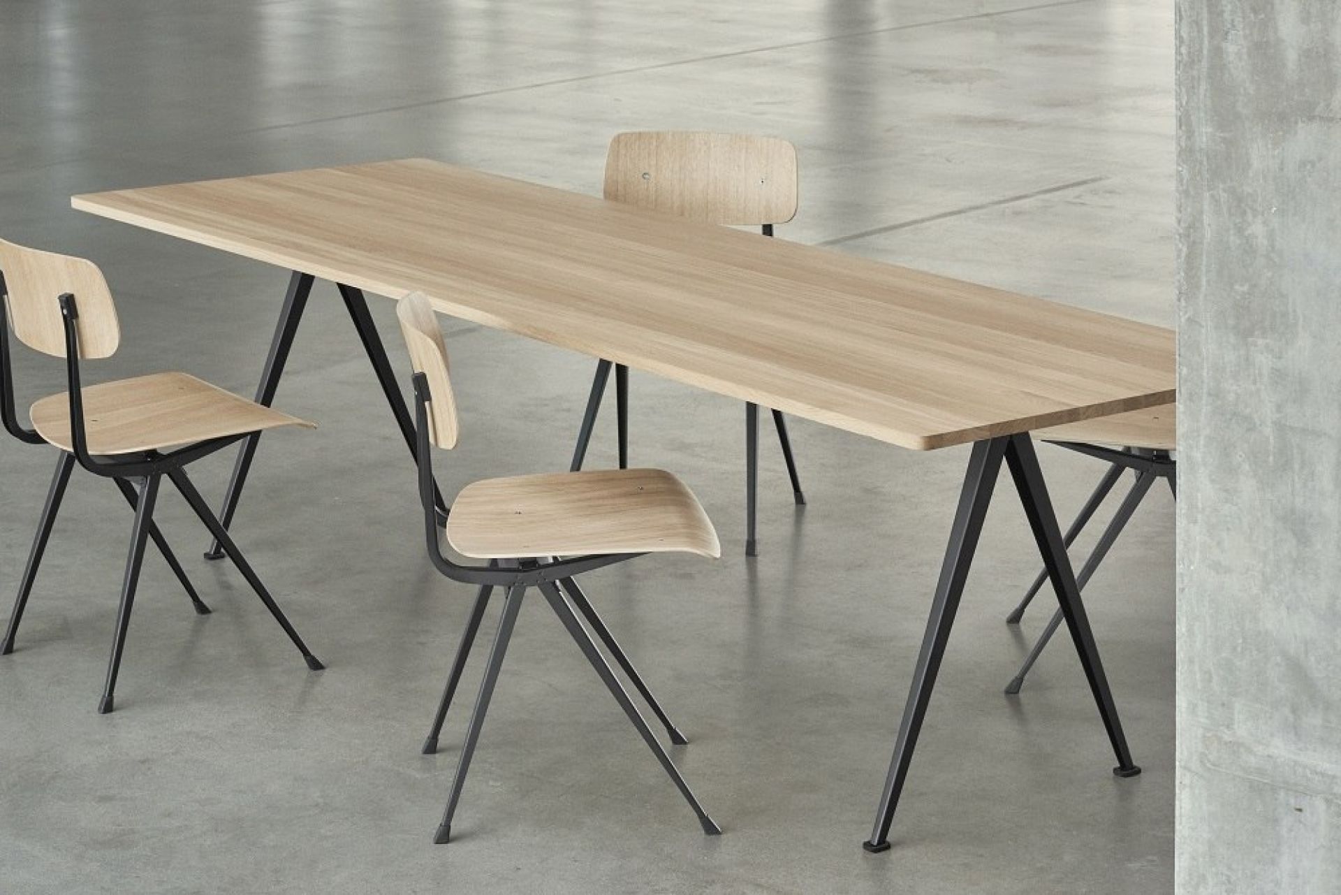 Pyramid Table 02 Esstisch von Hay mit Holzplatte und schwarzen Stahlbeinen, umgeben von Stühlen.