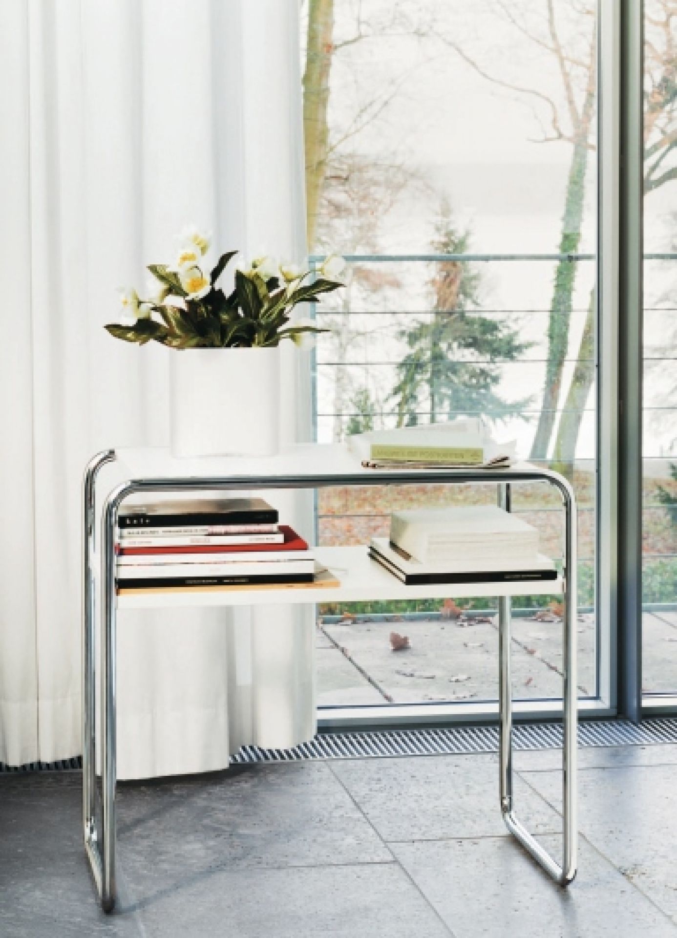 Thonet B 9 d/1 Beistelltisch mit Fachboden, Stahlrohr und weißen Ablageflächen, Bücher und Dekoration.