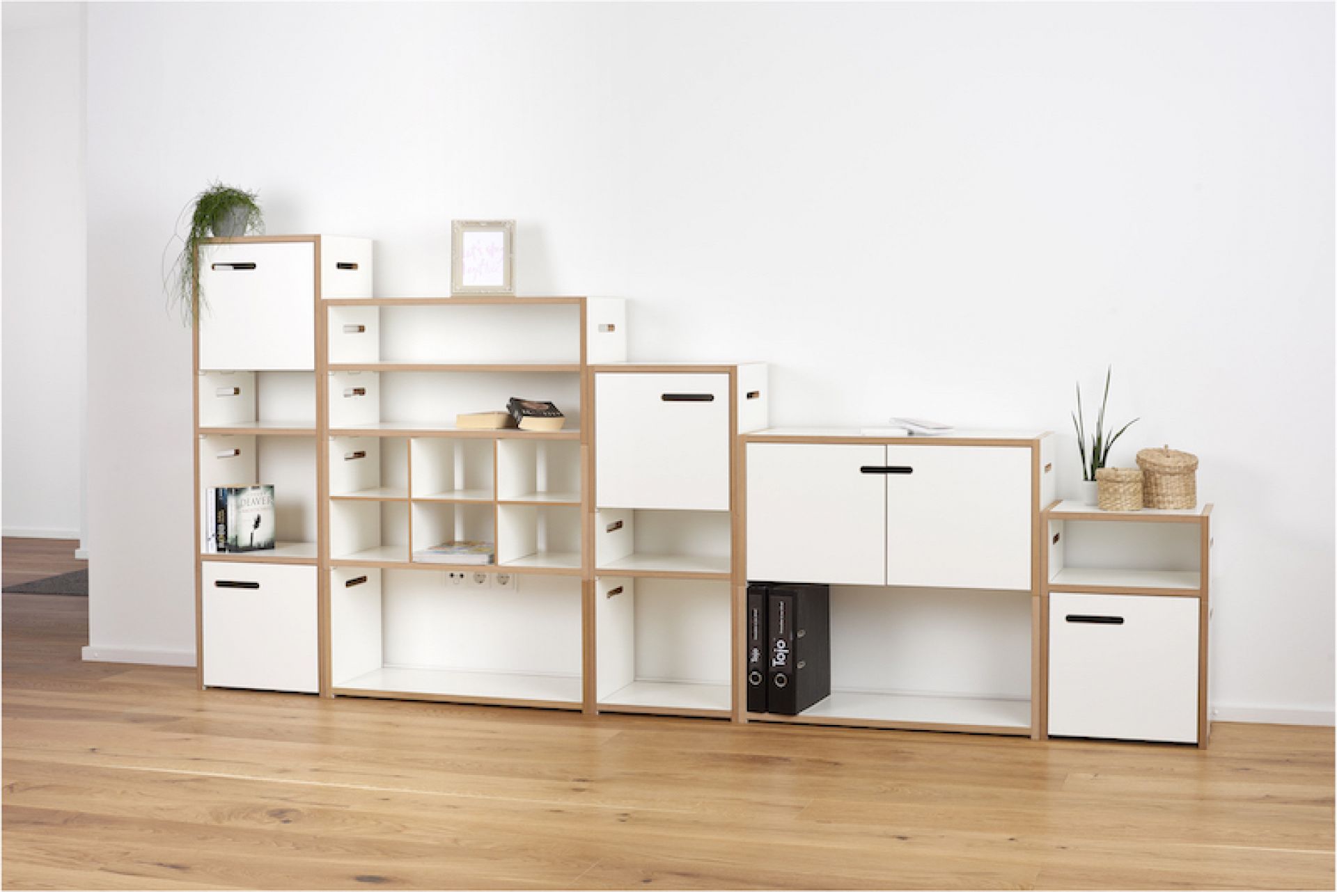 Tojo Hochstapler Regalsystem: Weißes modulares Regal mit Fächern, Schubladen und Schranktüren im Wohnzimmer.