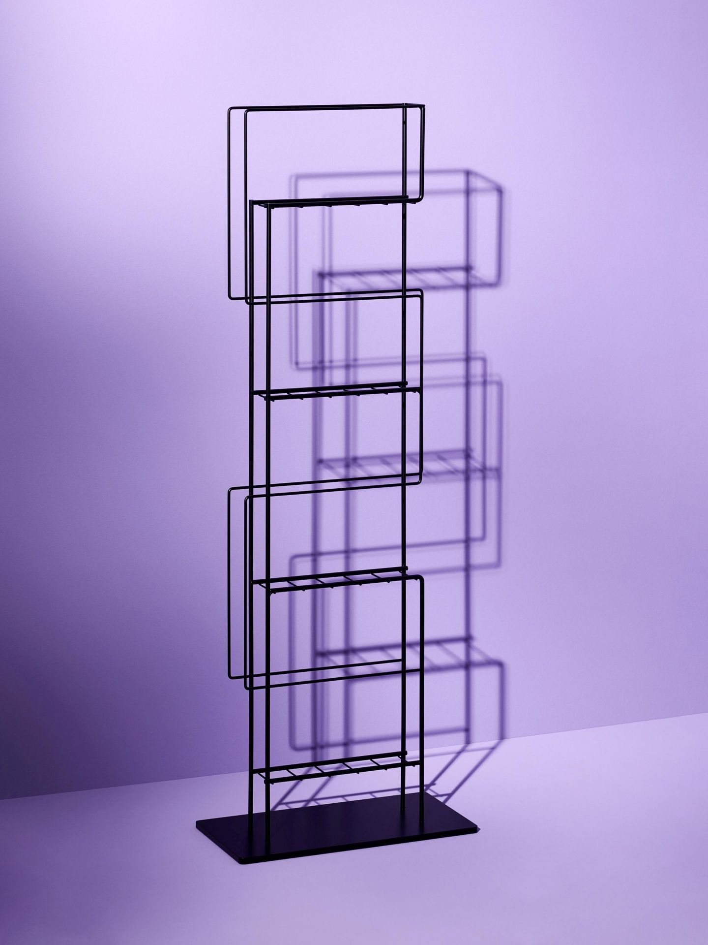 Schwarzer Schönbuch Zeitungsständer aus Metall mit mehreren Fächern vor lila Hintergrund. Design Zeitungsregal für Zeitschriften.