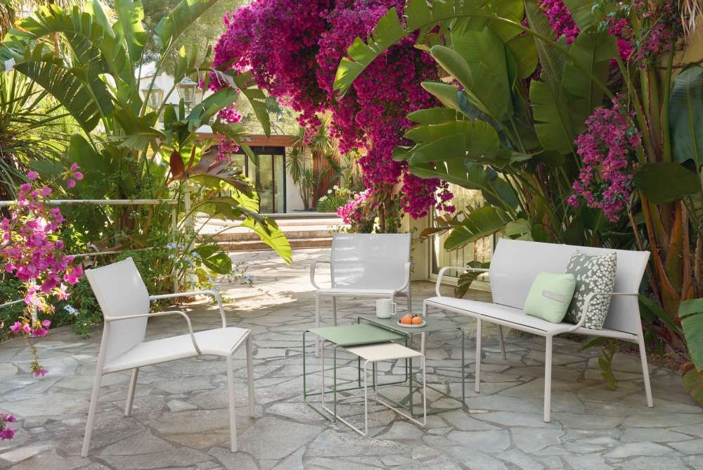 Weiße Cadiz 2-Sitzer Gartenbank von Fermob mit Stühlen und Beistelltischen im Außenbereich.