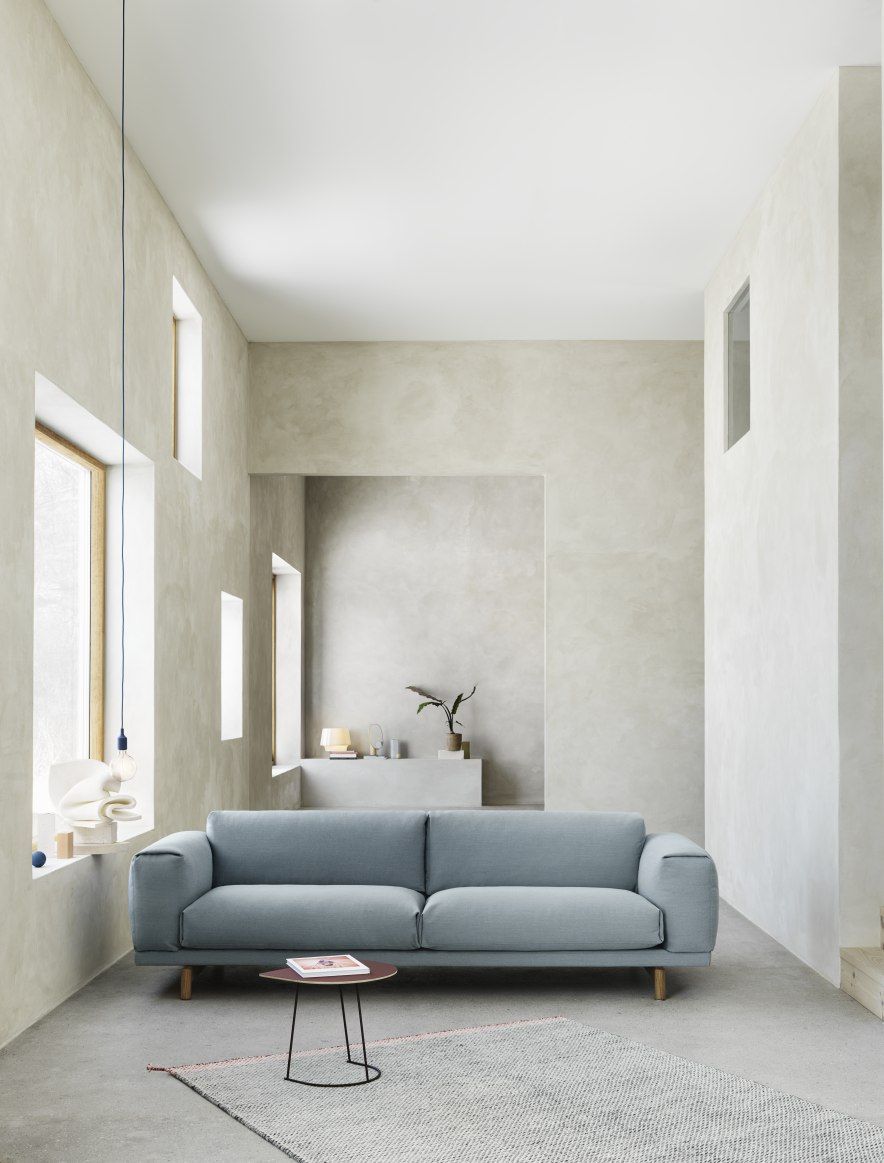 Helles Interieur mit blauem Muuto Rest Sofa, kleinem Tisch und Teppich. Modernes skandinavisches Design.