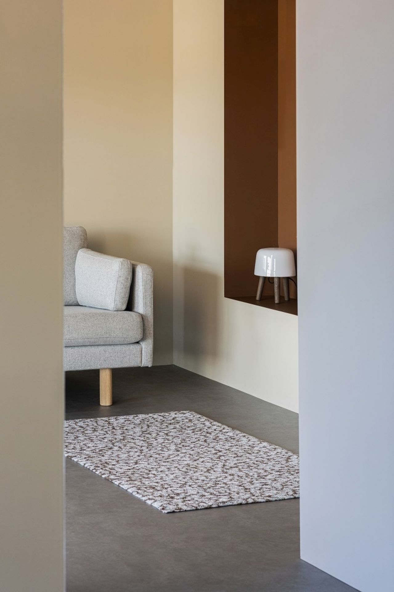 Heymat Grain Sandstone Fußmatte im Innenraum, mit Sofa und Lampe im Hintergrund. Hochwertige, moderne Fußmatte.