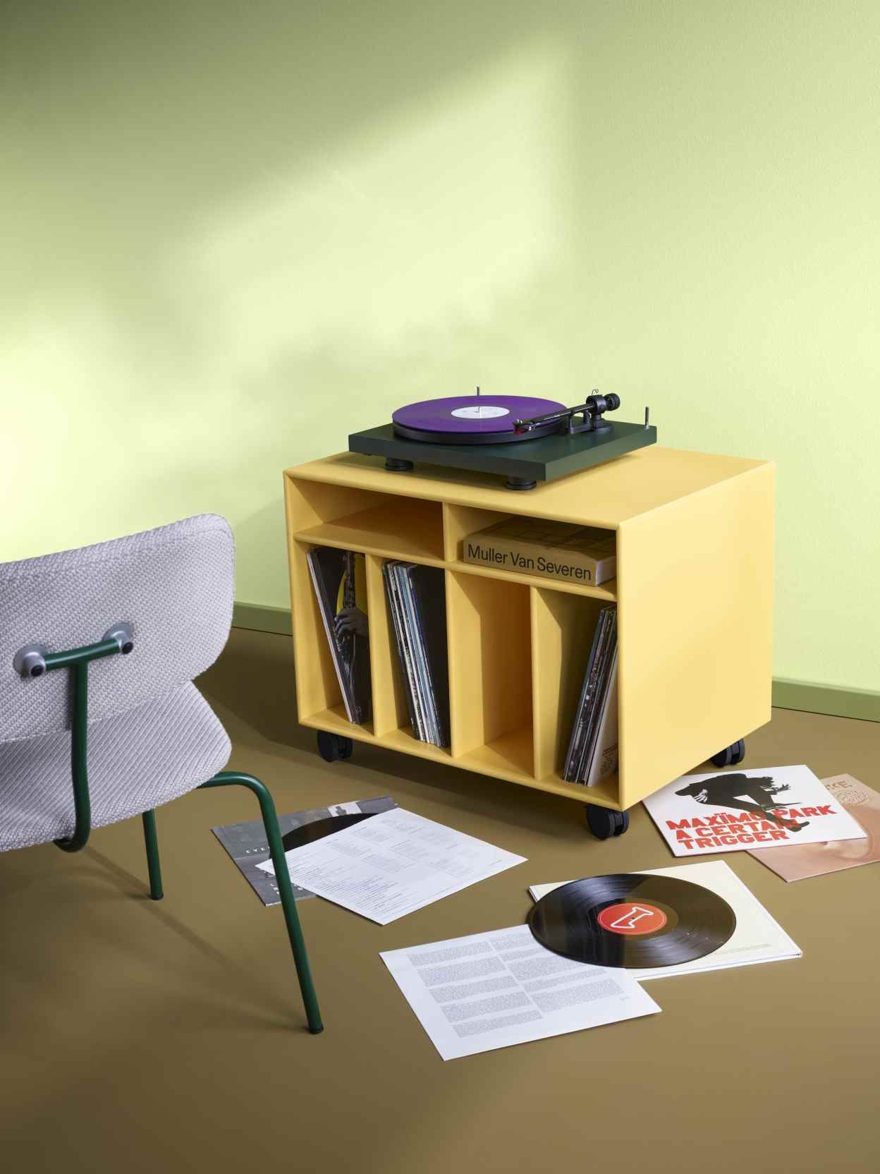 Gelbe Spin Schallplattenaufbewahrung mit Schallplatten, Plattenspieler und Stuhl in einem Wohnzimmer.