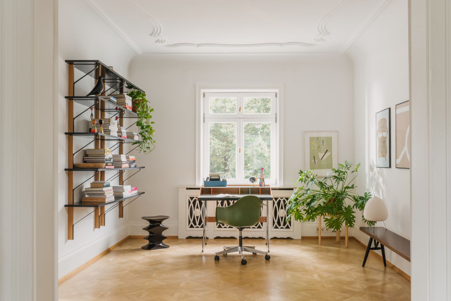 Büro mit Eames Plastic Arm Chair PACC von Vitra, Schreibtisch und Regalen in hellem Raum.