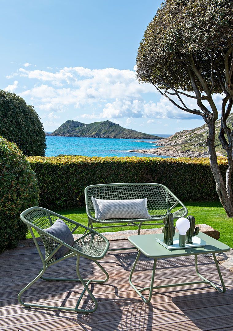 Grüne Fermob Sixties Gartenmöbel: Bank, Sessel und Tisch auf Holzterrasse mit Meerblick. Outdoor-Möbel für Garten und Balkon.