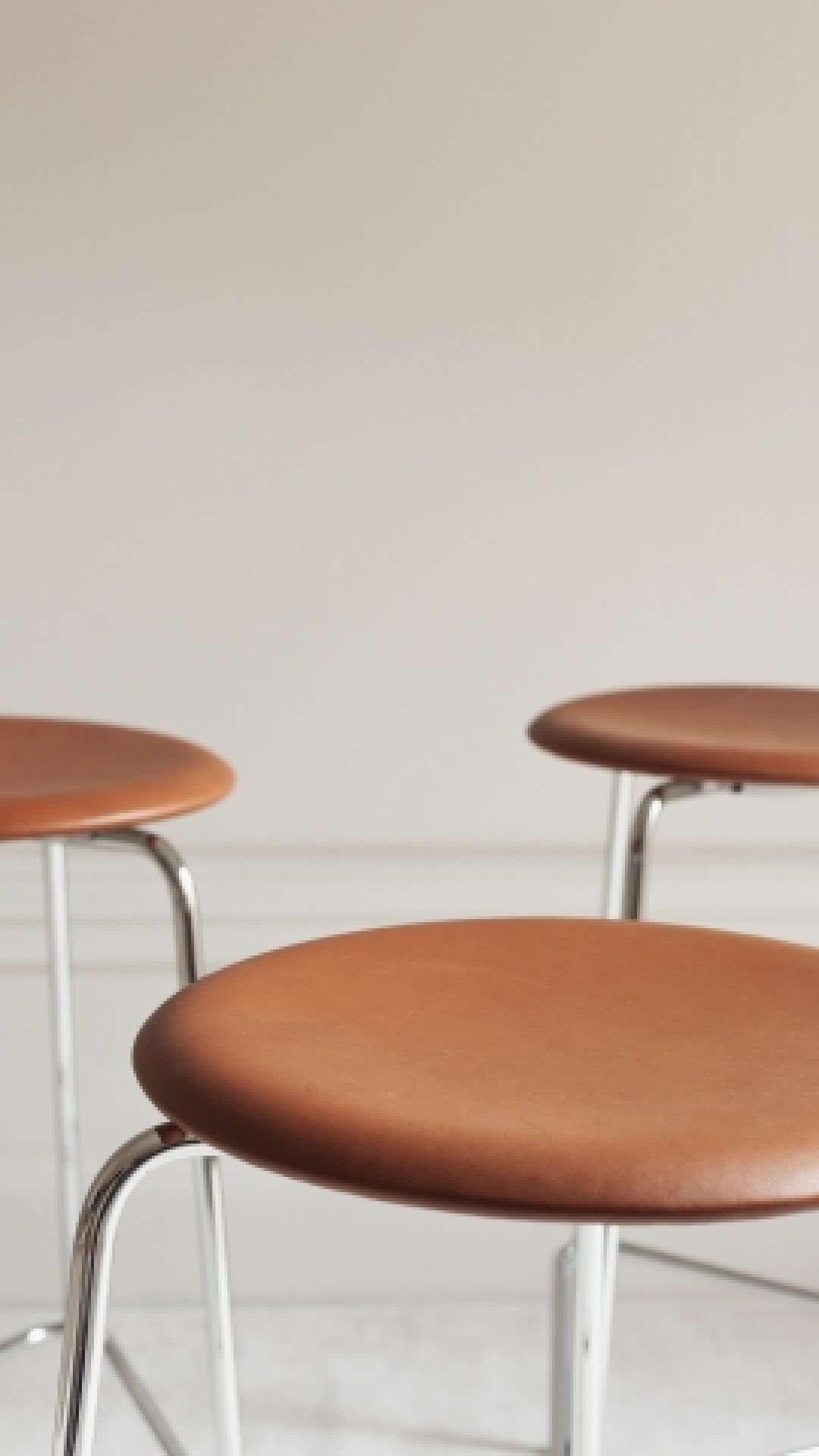 Nahaufnahme von drei Dot Hockern von Fritz Hansen mit braunen Ledersitzen und Chromgestell.