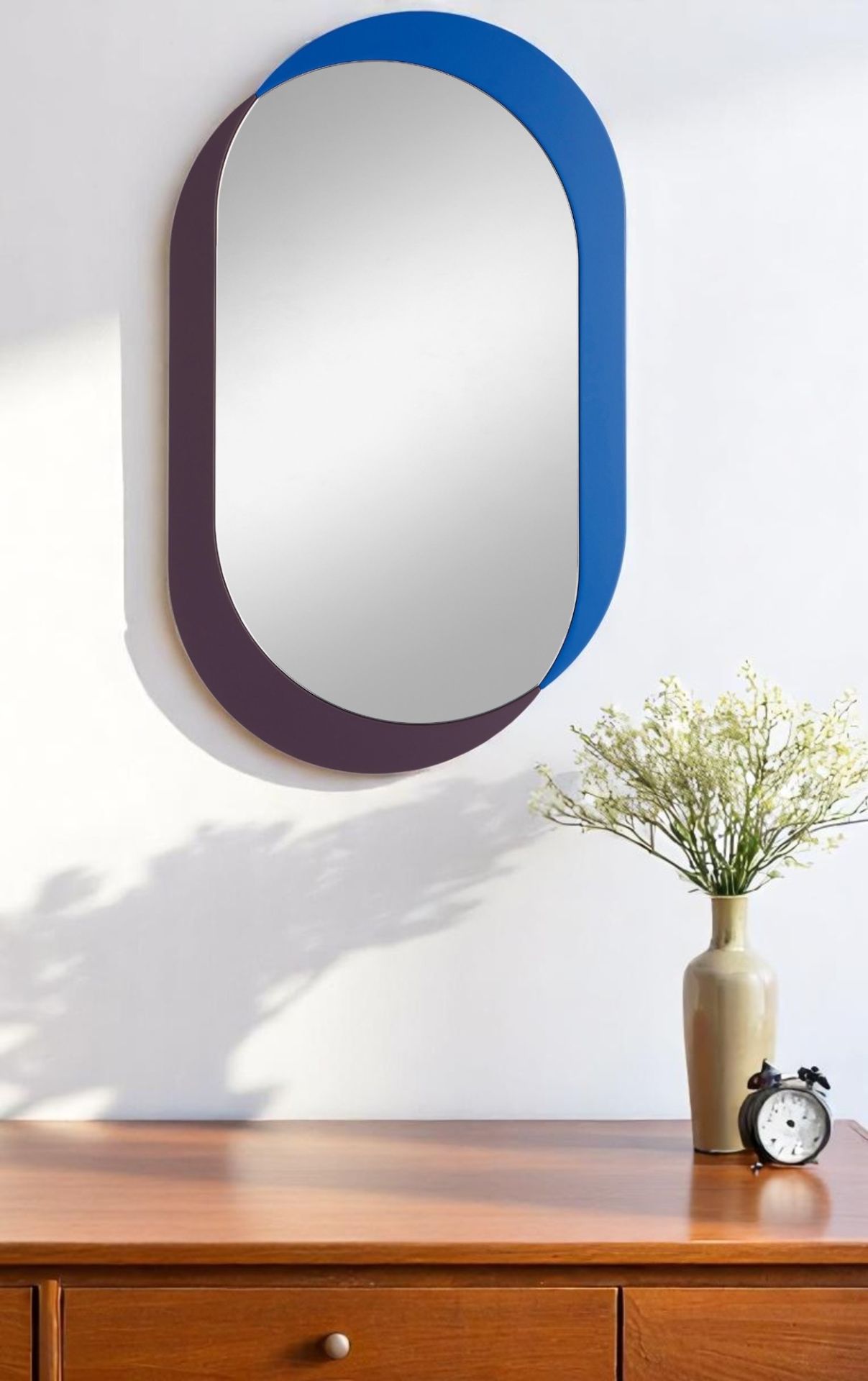 Ovaler Kimo Wandspiegel von Schönbuch mit blauem und auberginefarbenem Rahmen über einer Kommode.
