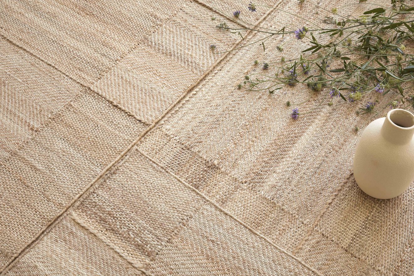 Beiger Roots Teppich mit geometrischem Muster, kombiniert mit einer Vase und Blumen.