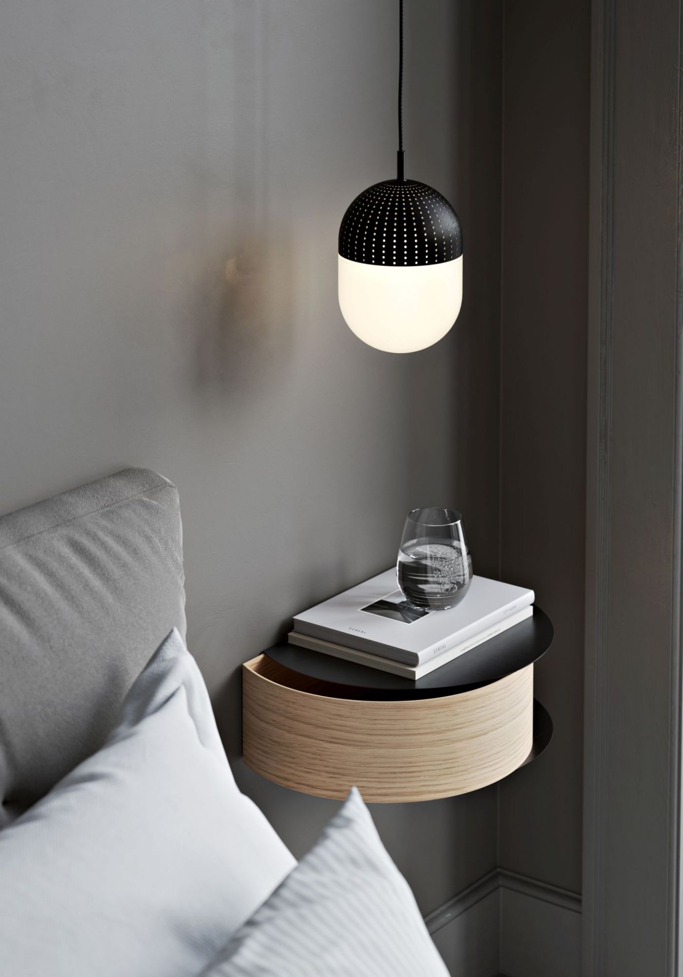 Nahaufnahme des Wallie Wandschubladen Regals von Woud in Grau-Beige neben einem Bett mit Lampe.
