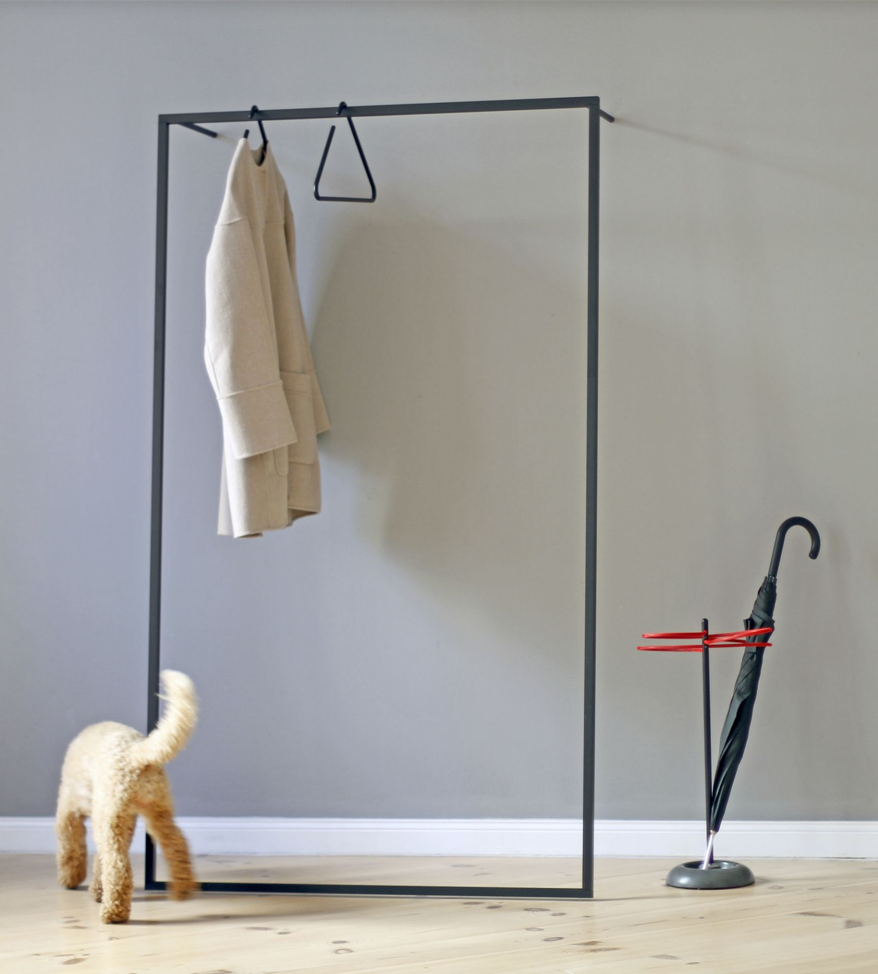 Leano Anlehngarderobe von Roomsafari mit Mantel, Schirmständer und Hund im Flur. Moderne Garderobenlösung.