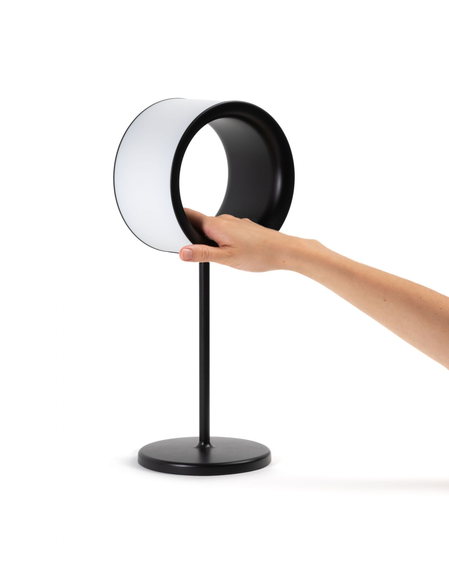 Lost Tischleuchte von Magis, schwarzes Gestell, halbrunder Lampenschirm, Hand berührt die Lampe.